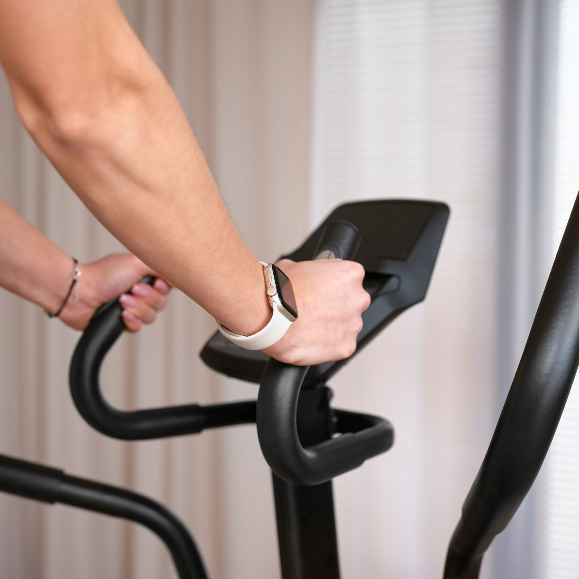 Eine Person trainiert drinnen auf einem schwarzen Crosstrainer und trägt eine weiße Fitnessuhr.