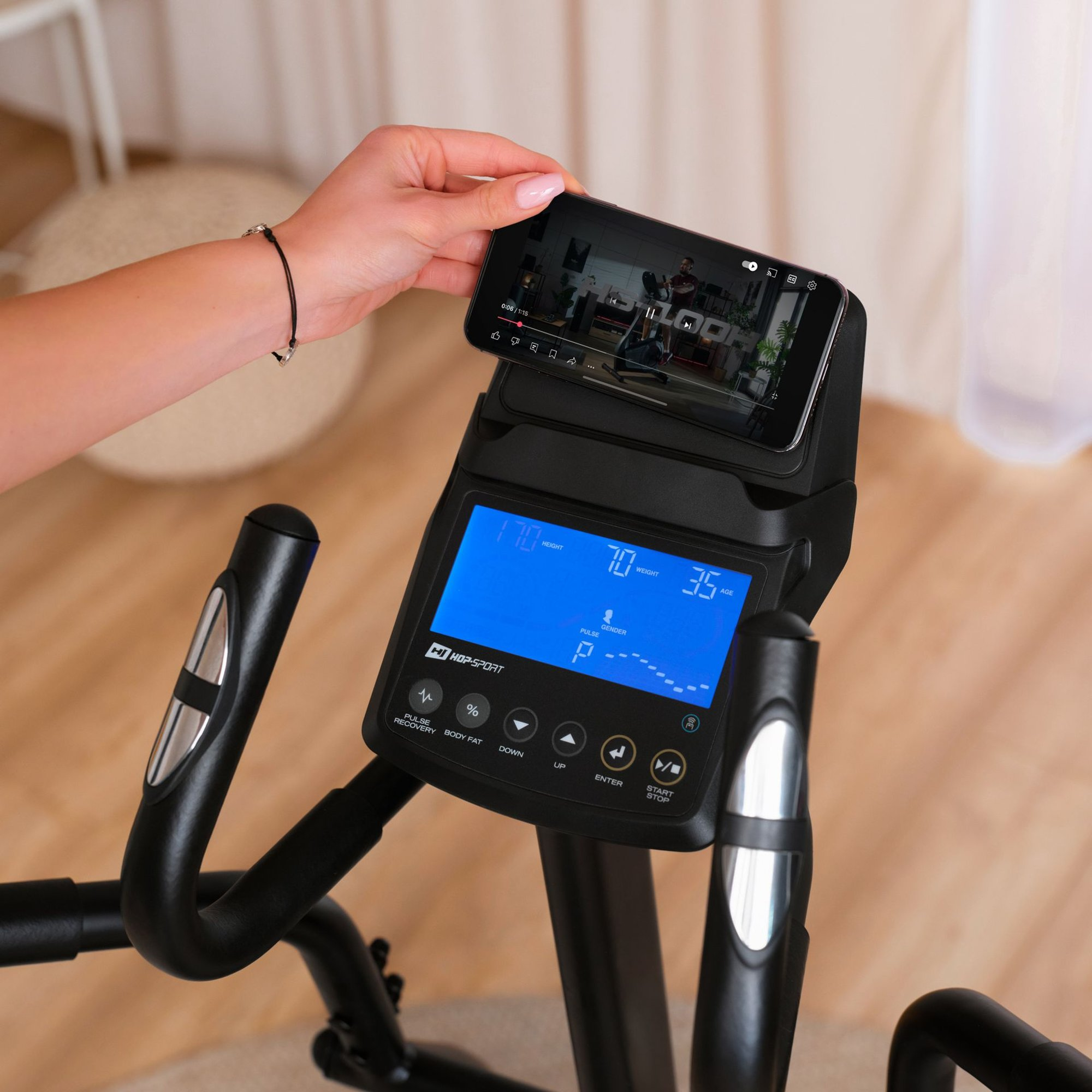 Hand platziert ein Smartphone auf dem Display eines Heimtrainers mit blauer Anzeige.