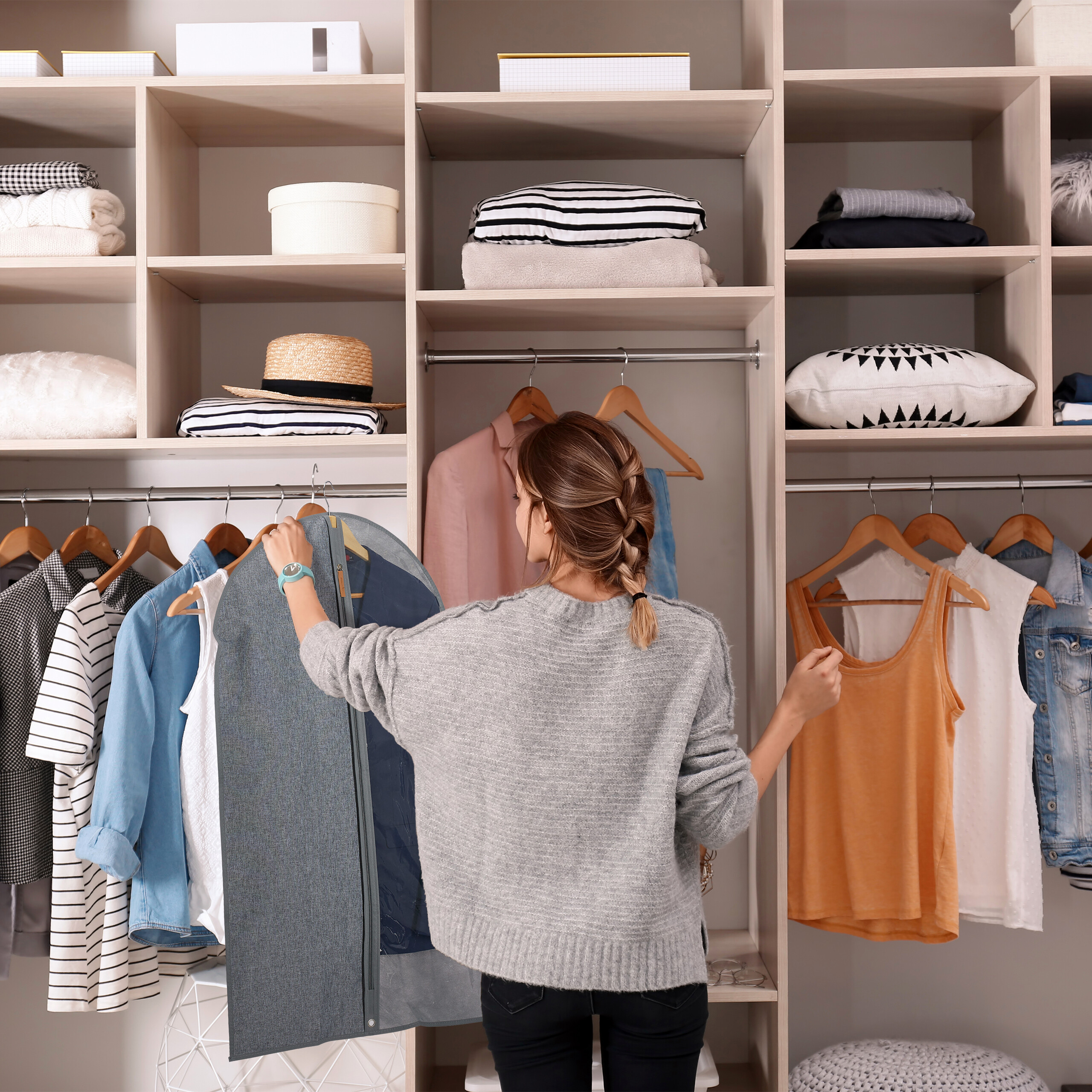 Frau mit geflochtenem Haar hält Kleidersack vor großem, gut gefülltem Kleiderschrank.