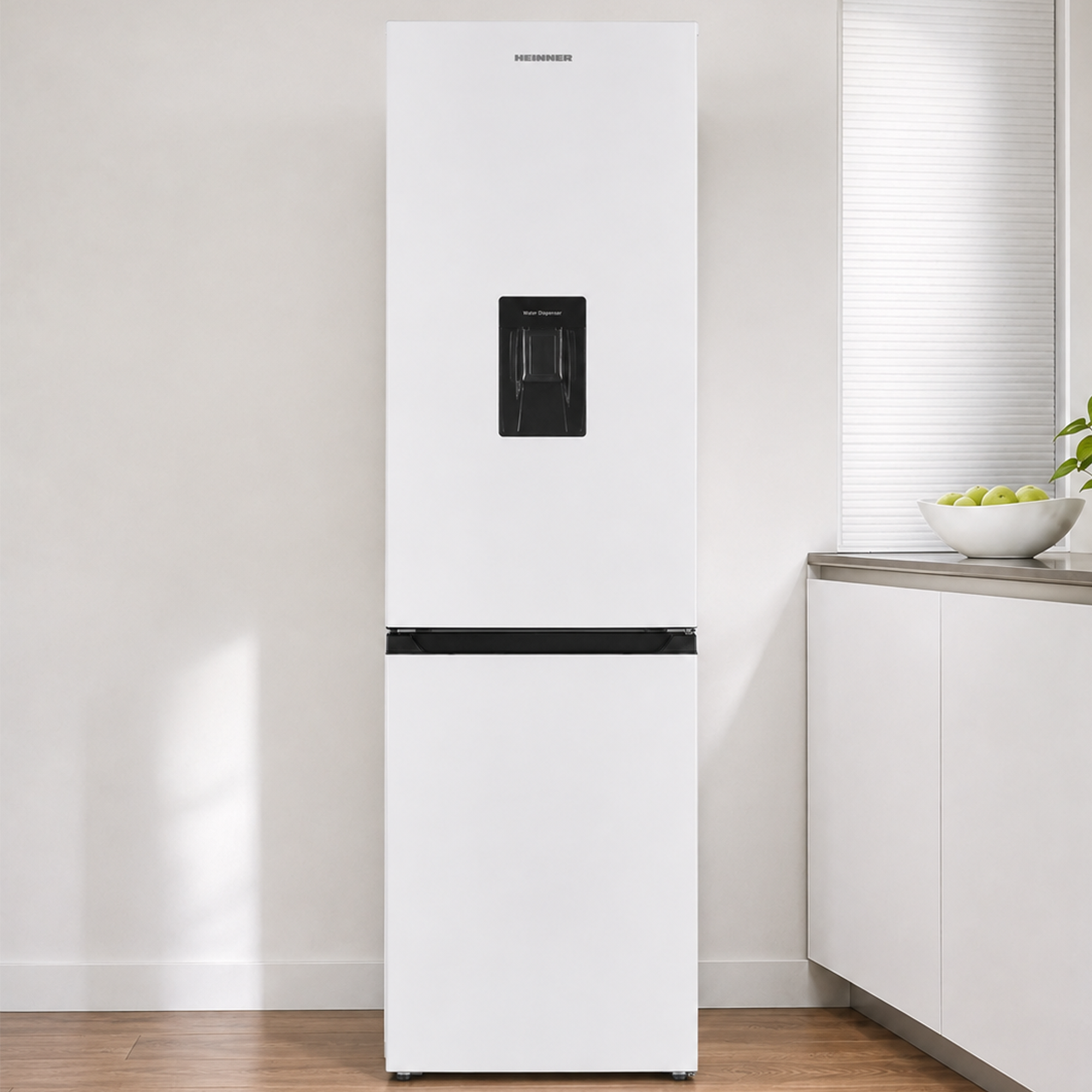 Un réfrigérateur blanc Heinner avec distributeur d'eau noir se trouve dans une cuisine moderne près d'une fenêtre.