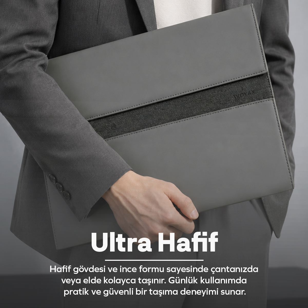 Gri takım elbiseli bir kişi, gri duvar önünde koyu şeritli gri bir laptop çantası tutuyor.