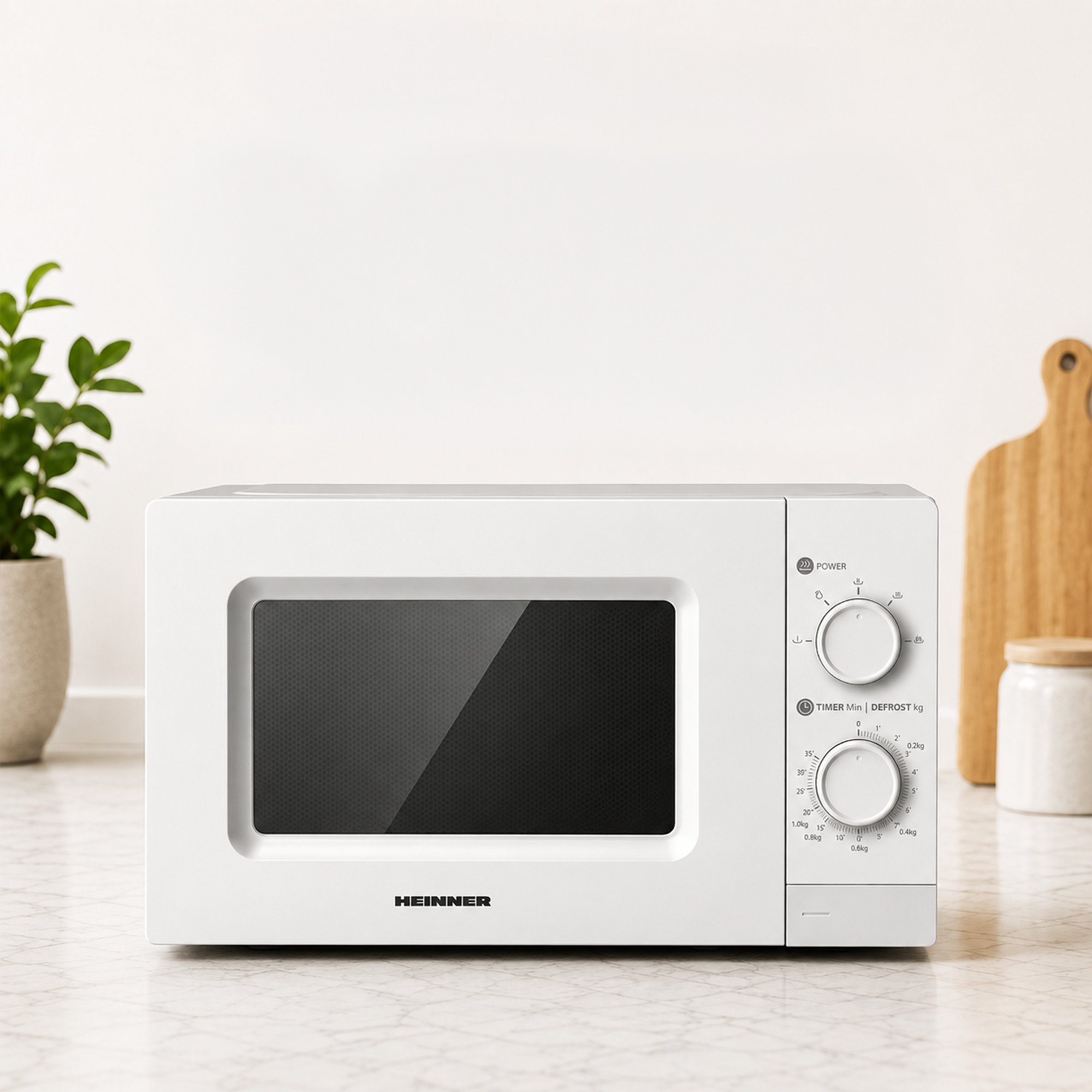 A white Heinner microwave with two rotary dials sits on a kitchen counter against a white wall.