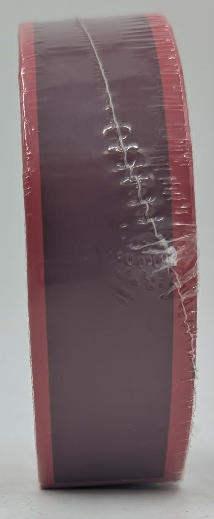 Eine Rolle rotes und dunkelrotes Klebeband, fest in Klarsichtfolie verpackt.