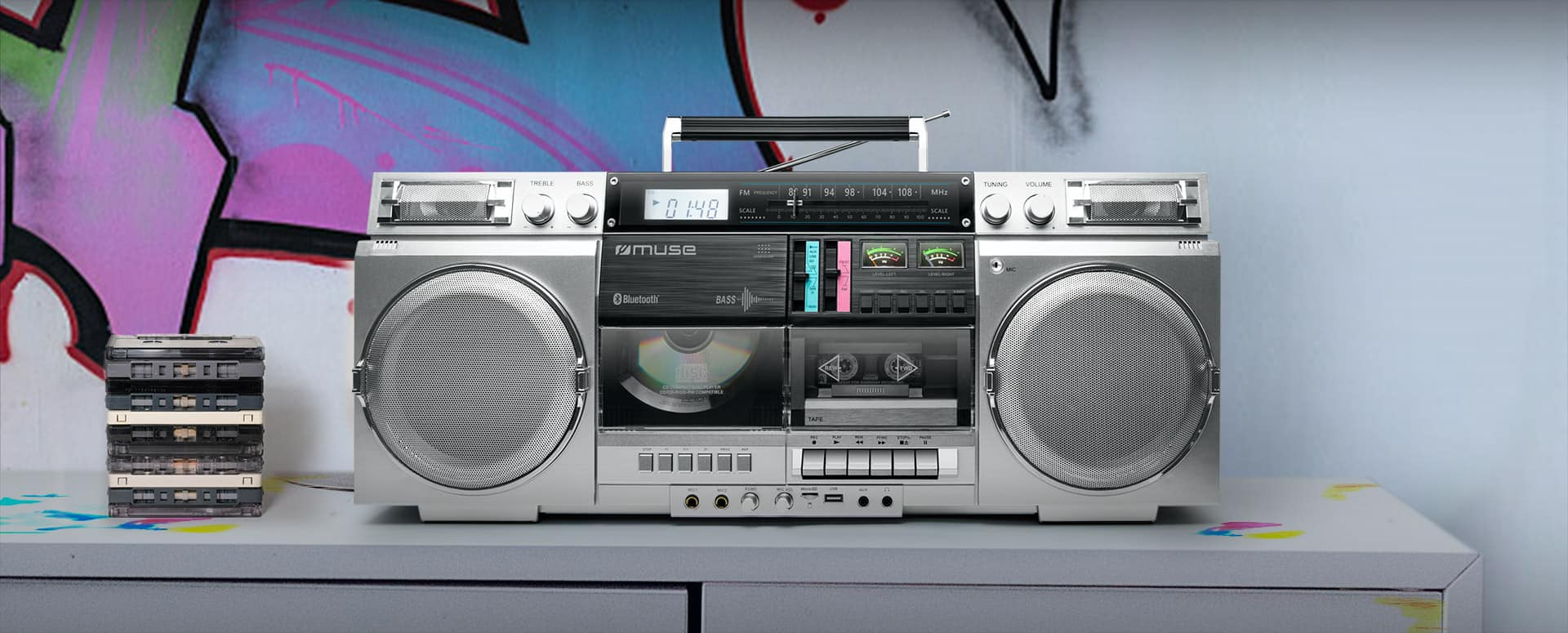 Eine silberne Retro-Boombox mit zwei Lautsprechern und Kassettenfach steht auf einem Tisch mit Kassetten.