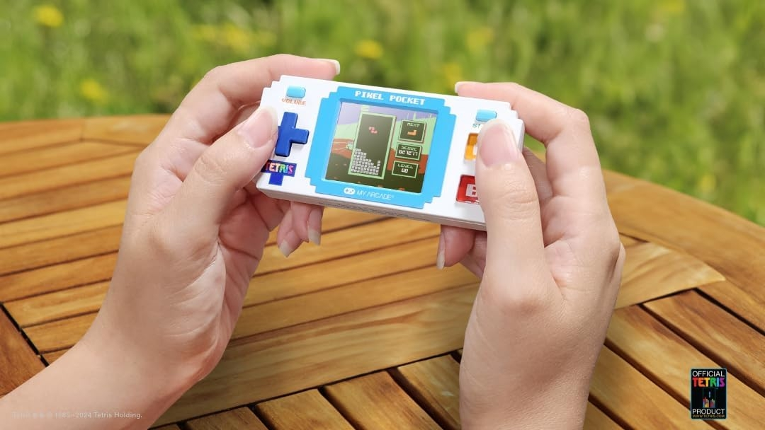 Hände halten eine weiße Pixel Pocket Tetris-Handheld-Konsole vor einem Holztisch.