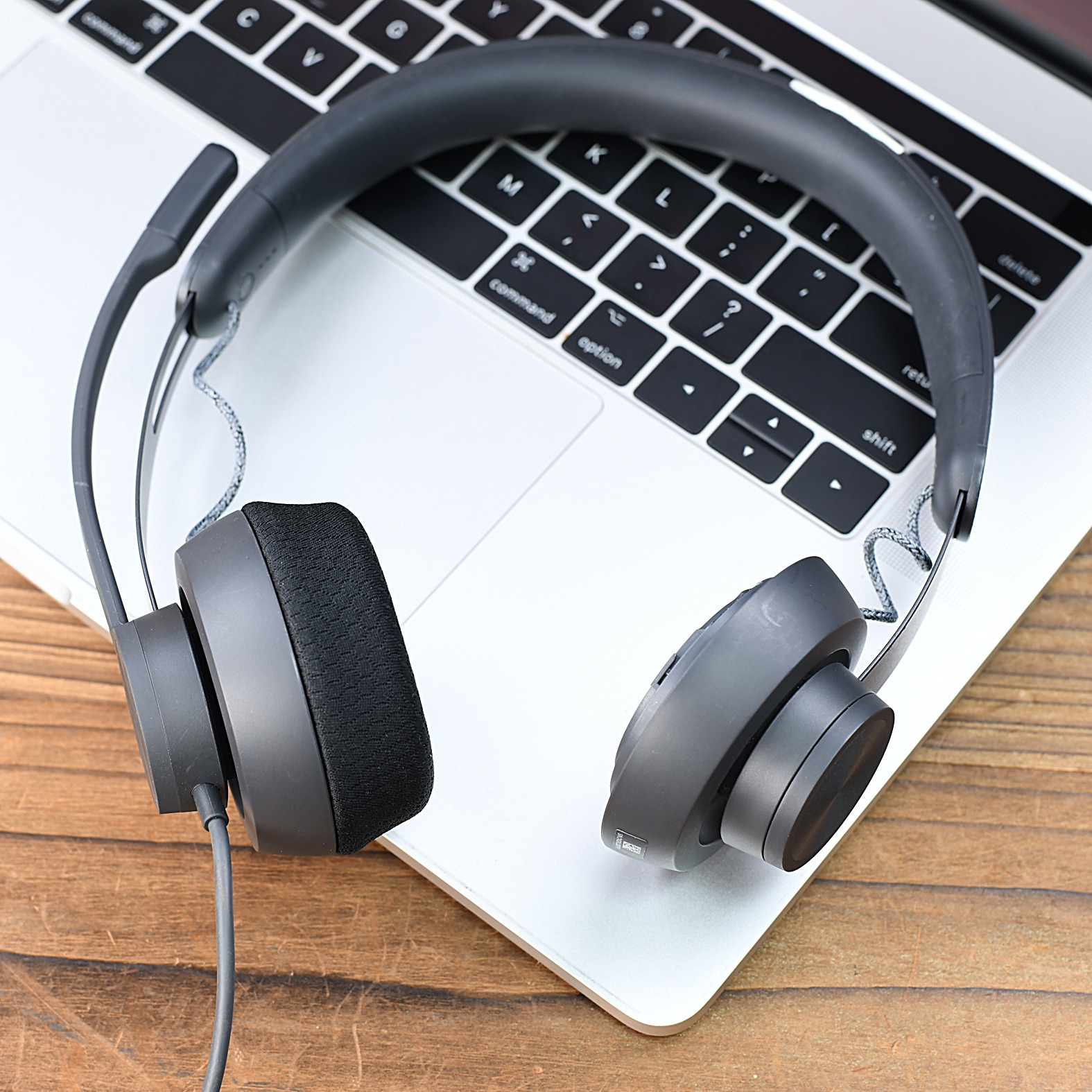 Schwarzes kabelgebundenes Büro-Headset auf einer silbernen Laptop-Tastatur auf einem Holzschreibtisch.