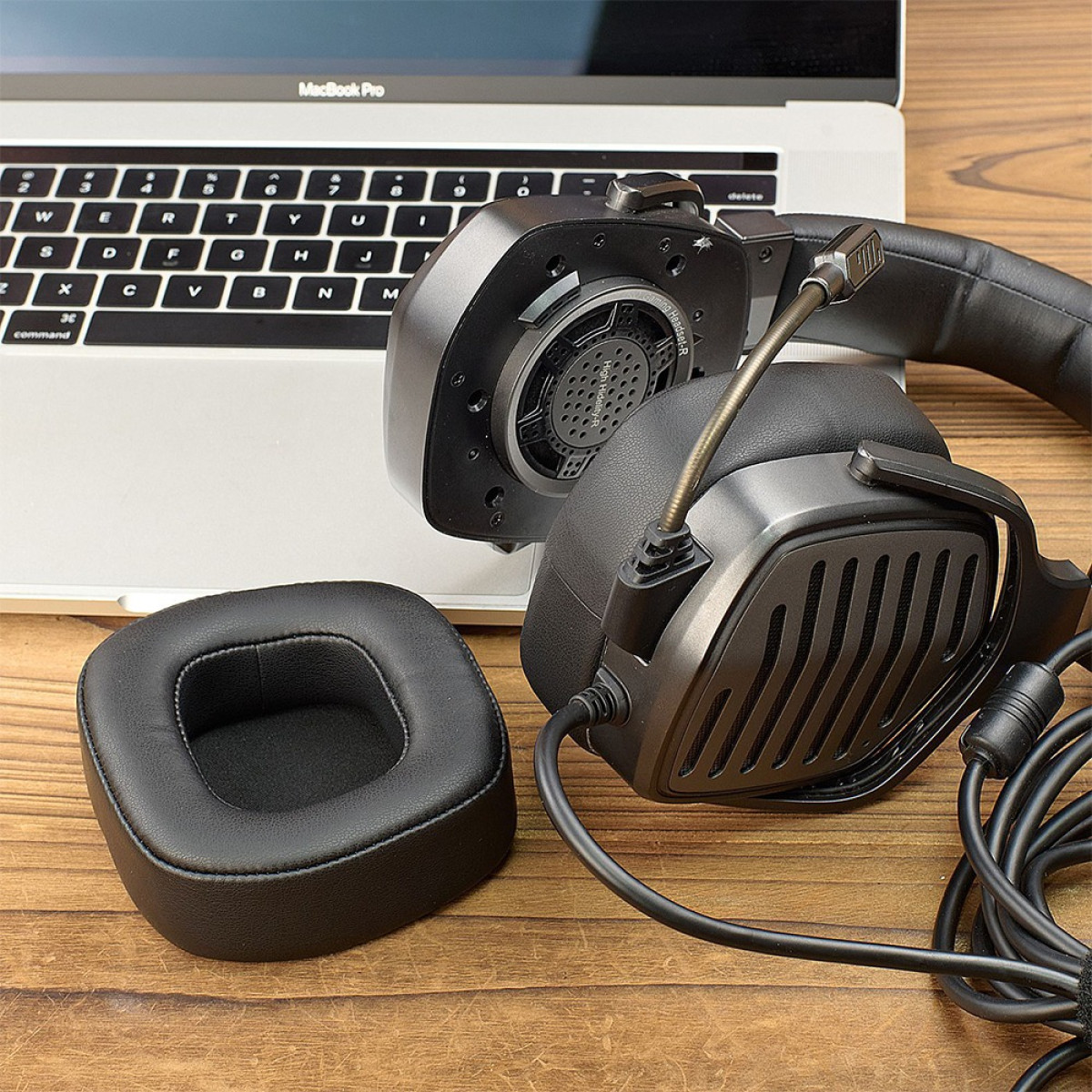 Schwarzes Gaming-Headset mit abnehmbarem Ohrpolster auf einem Holzschreibtisch neben einem Laptop.