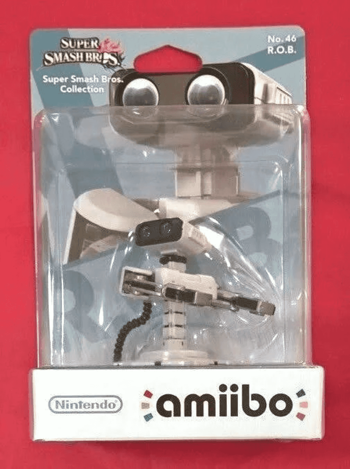 R.O.B. Super Smash Bros. Amiibo-Figur in ihrer ungeöffneten Plastikverpackung auf rotem Hintergrund.