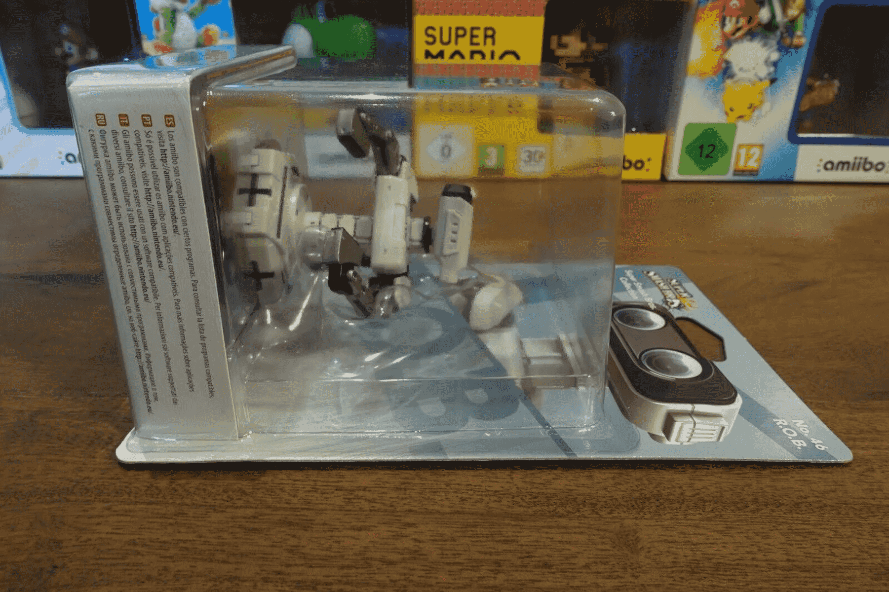 Verpackte R.O.B. Amiibo-Figur auf einem Holztisch, im Hintergrund weitere Spieleverpackungen.