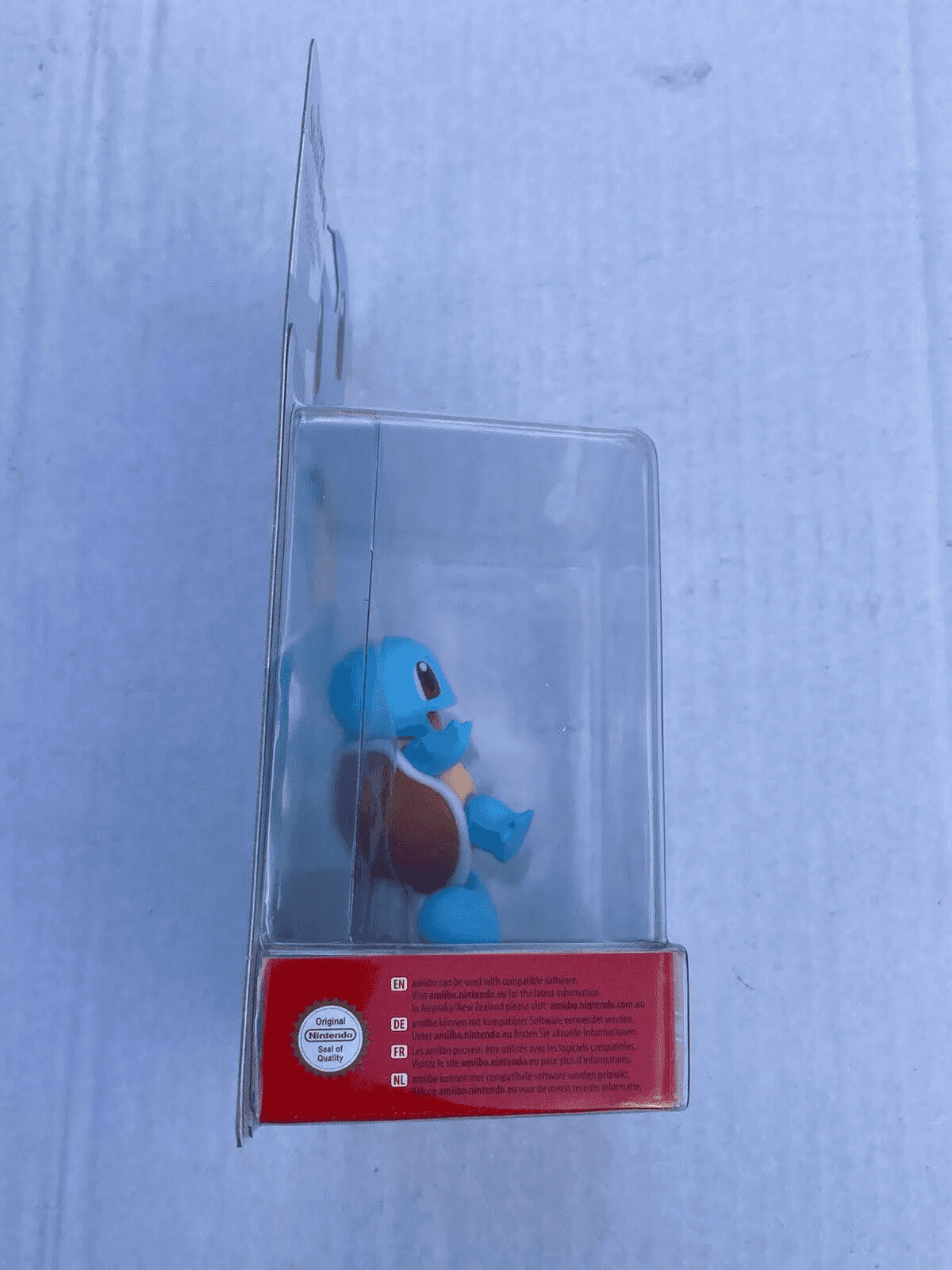 Vista lateral de una figura amiibo de Squirtle azul dentro de su embalaje de plástico y cartón.