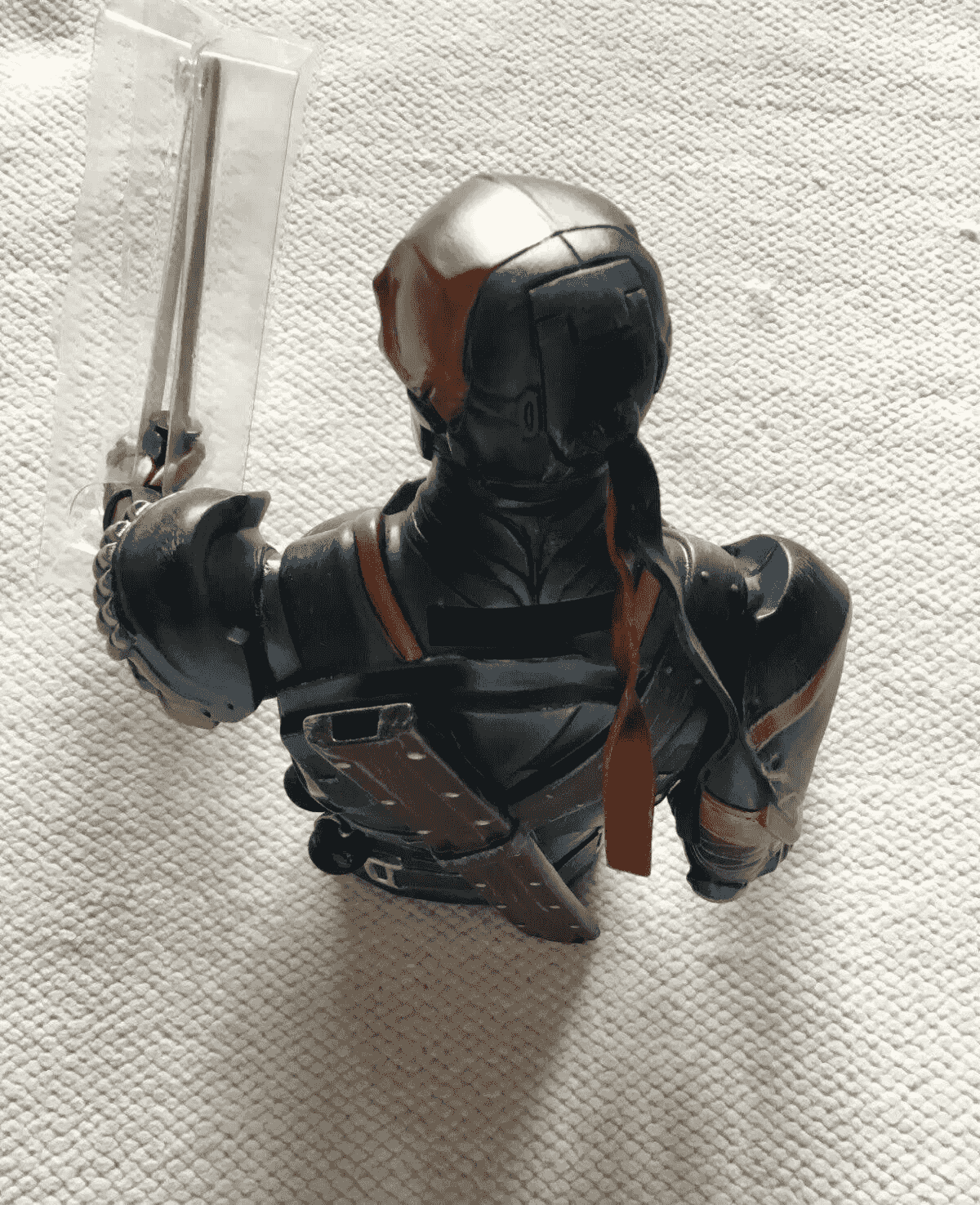 Rückansicht einer Deathstroke-Büste in Rüstung mit Schwert auf weißem Teppich.
