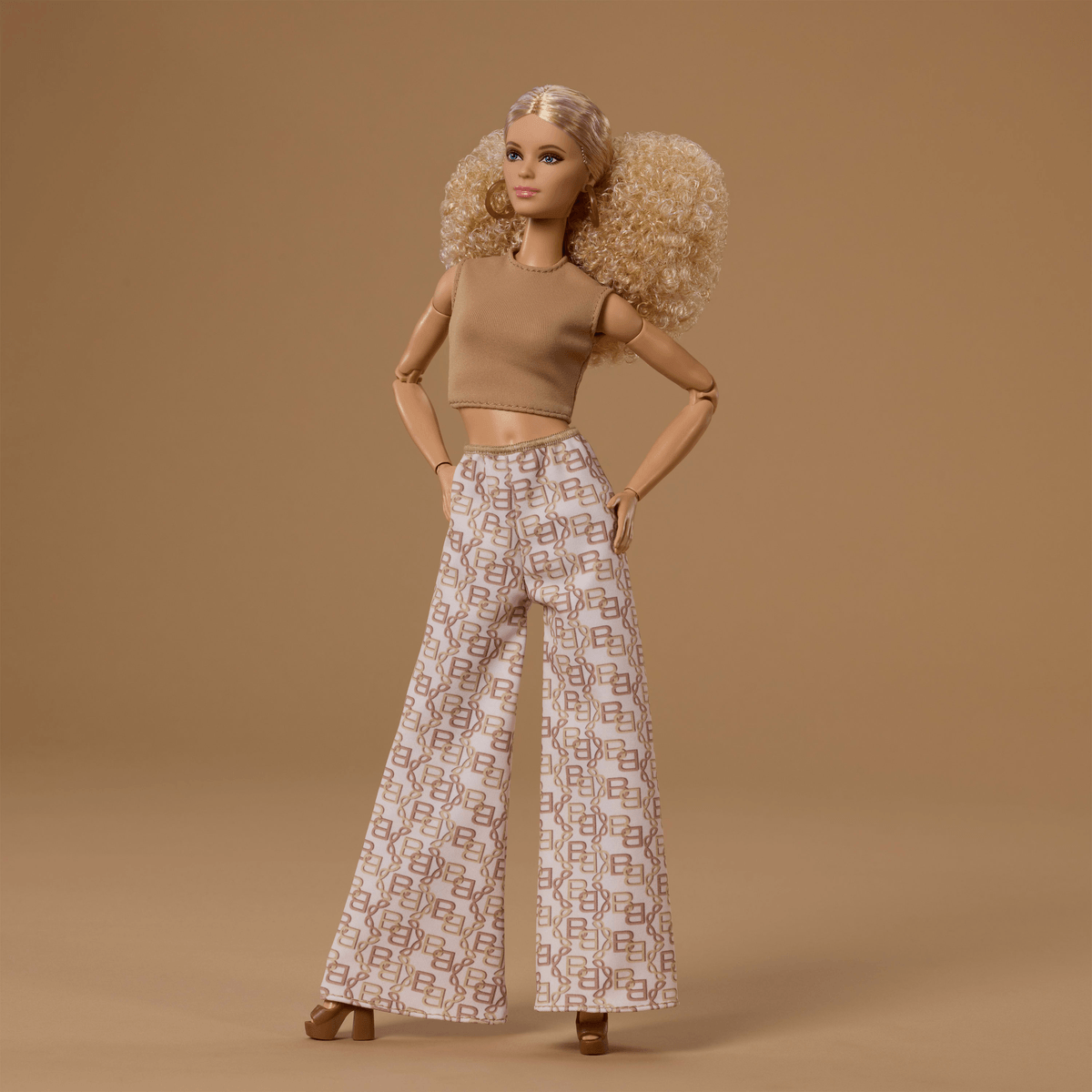 Modische blonde Puppe mit großem, voluminösem Haar, beigem Crop-Top und gemusterten Schlaghosen.
