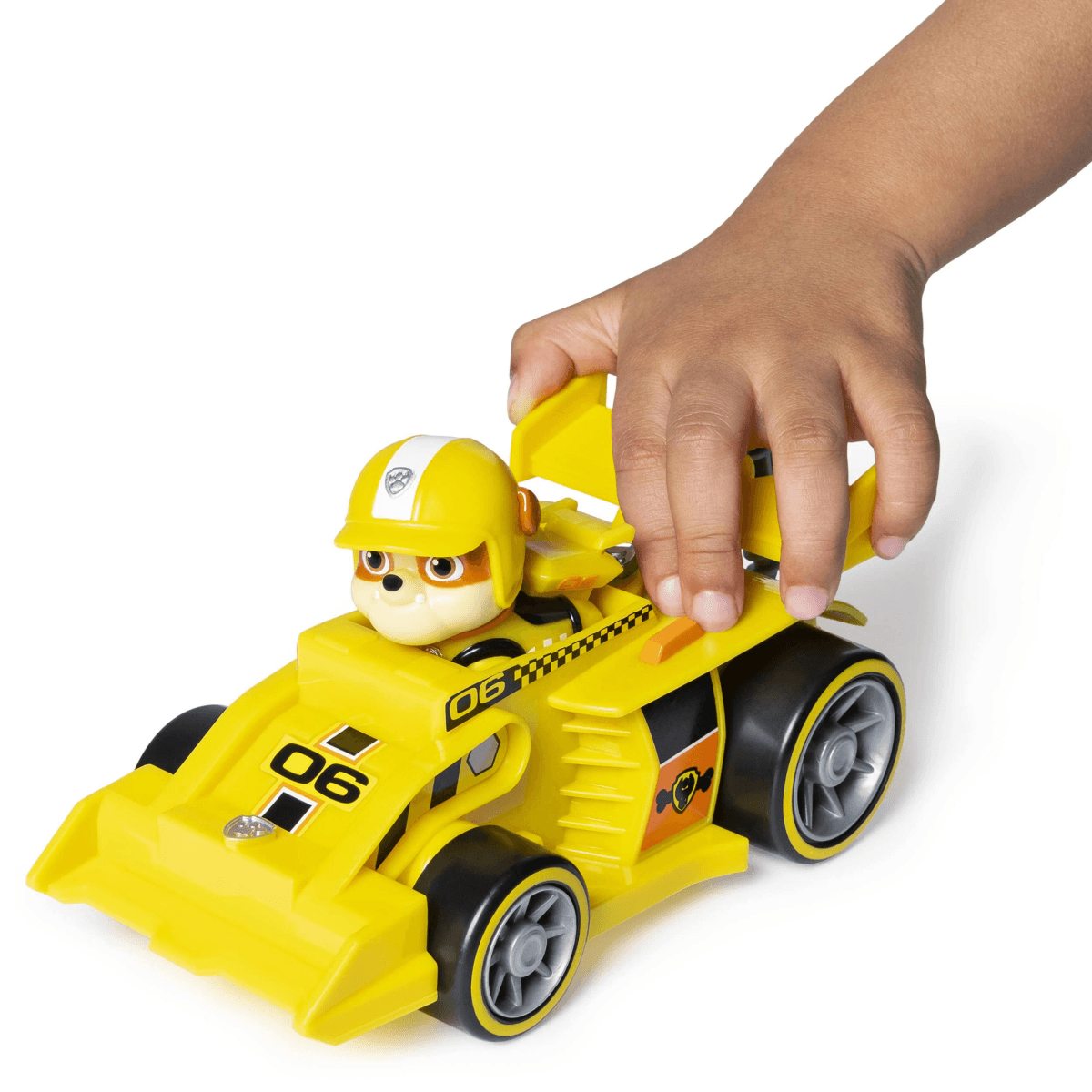 Eine Kinderhand spielt mit einem gelben Rennauto, gefahren von einem Zeichentrickhund mit Helm.
