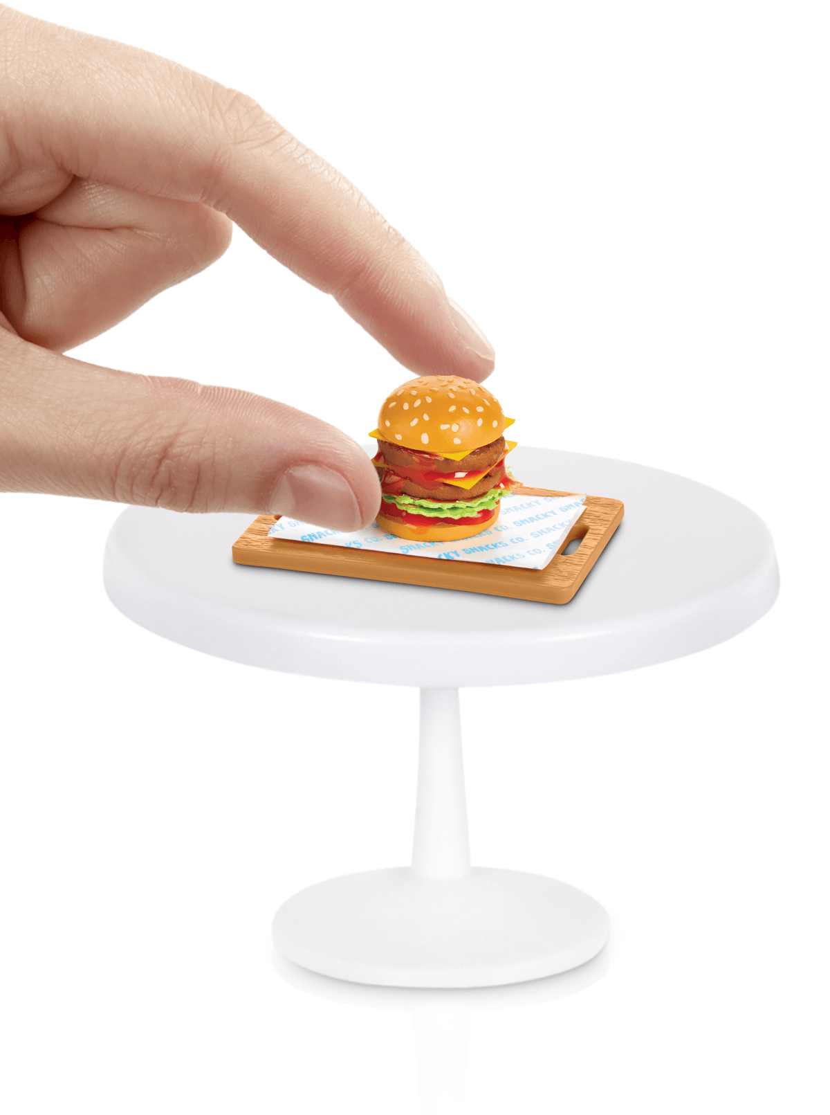 Eine Hand greift nach einem winzigen Burger auf einem Schneidebrett auf einem weißen Tisch.