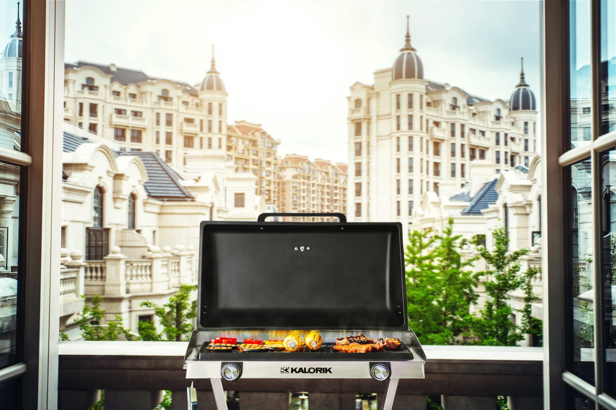 Grill Kalorik z warzywami i mięsem stoi na balkonie na tle klasycznego miasta.
