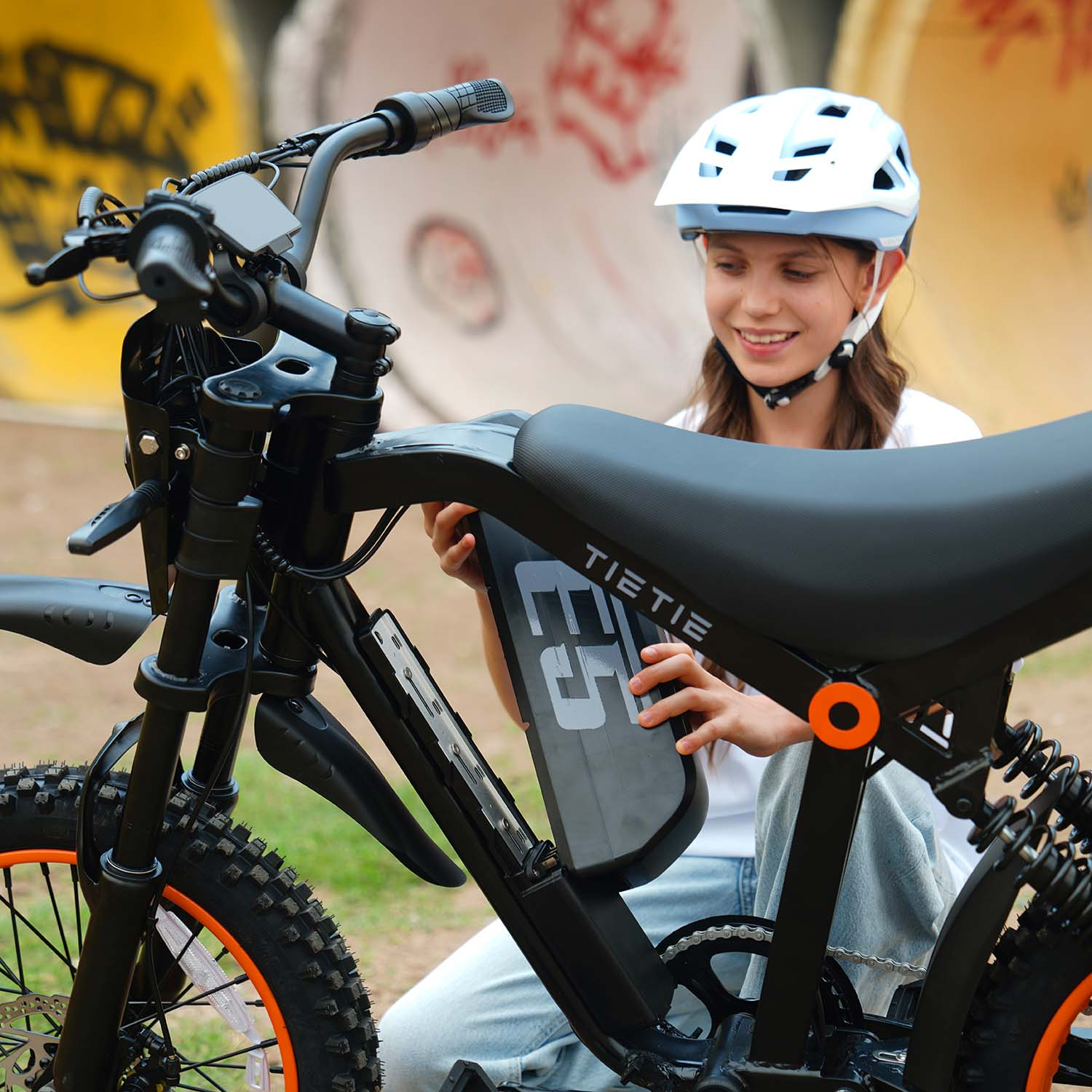 Dziewczyna w kasku wkłada akumulator do swojego czarnego e-bike'a.