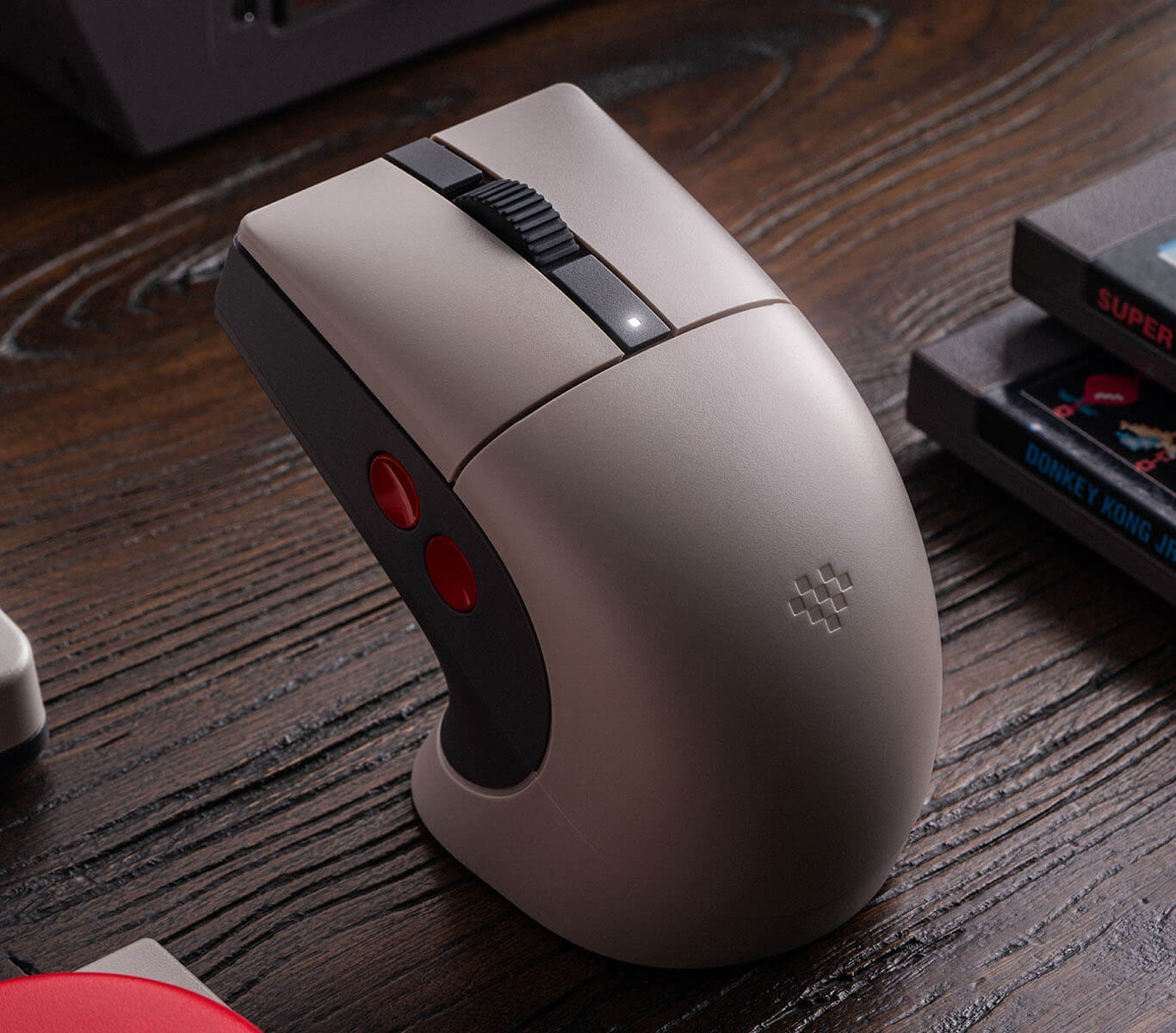 Un ratón de ordenador vertical de color beige y gris oscuro se encuentra en un escritorio de madera junto a cartuchos de videojuegos.