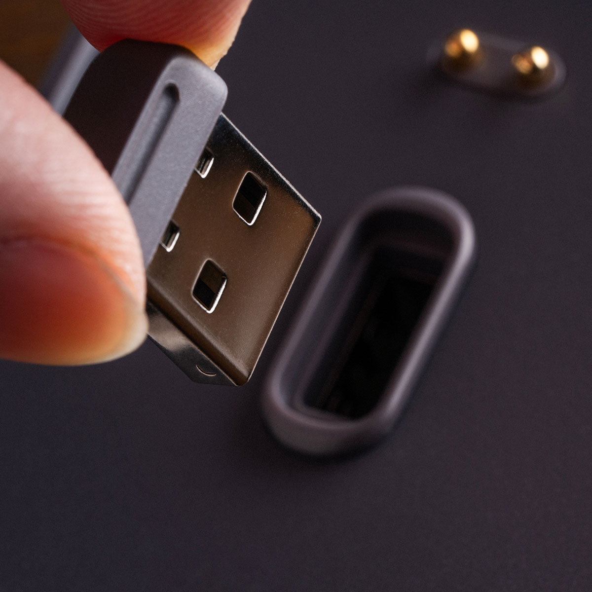 Una mano sostiene un conector USB acercándose a un puerto en una superficie oscura.
