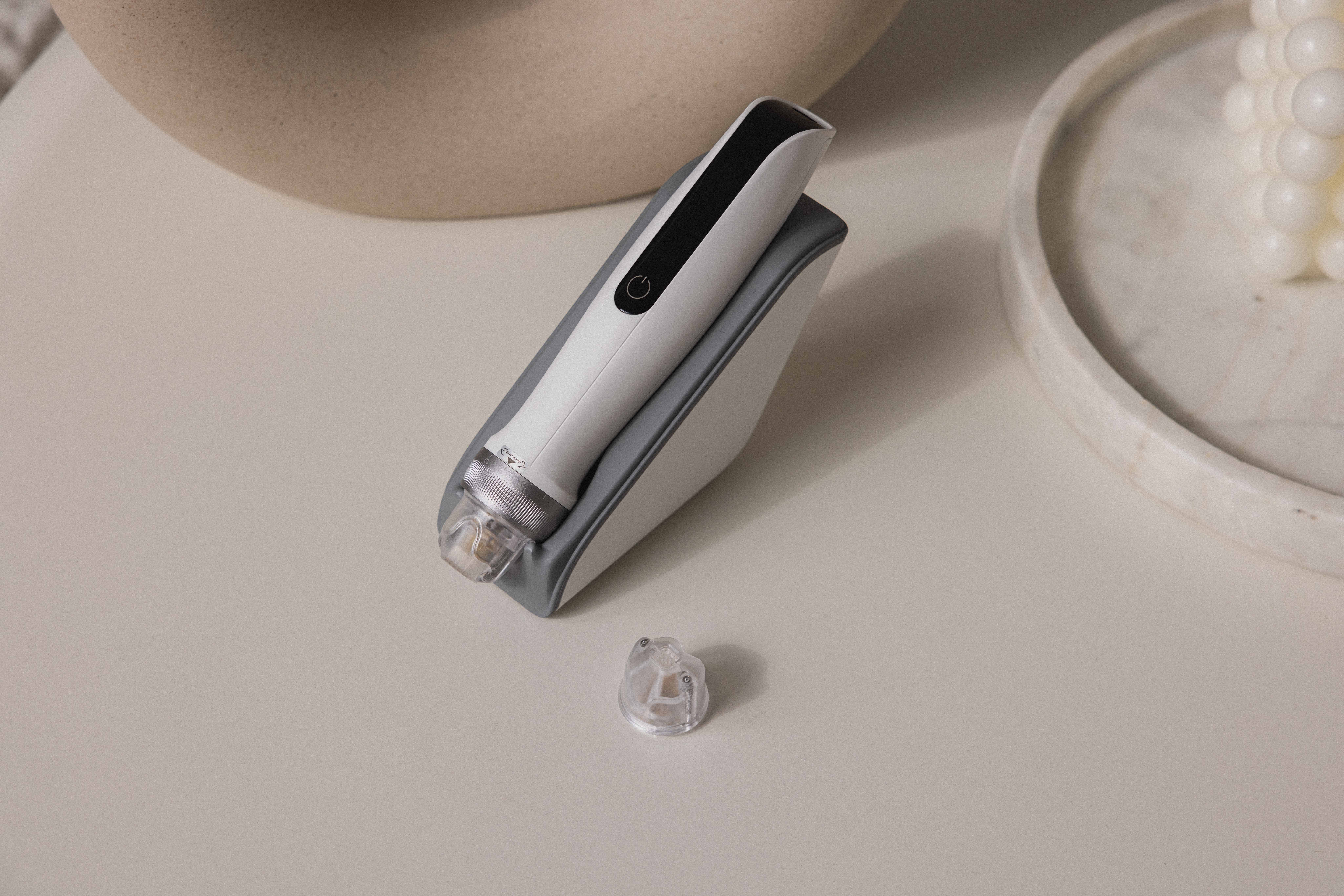 Un dispositivo per la cura della pelle bianco e grigio su un supporto chiaro, con un accessorio vicino.