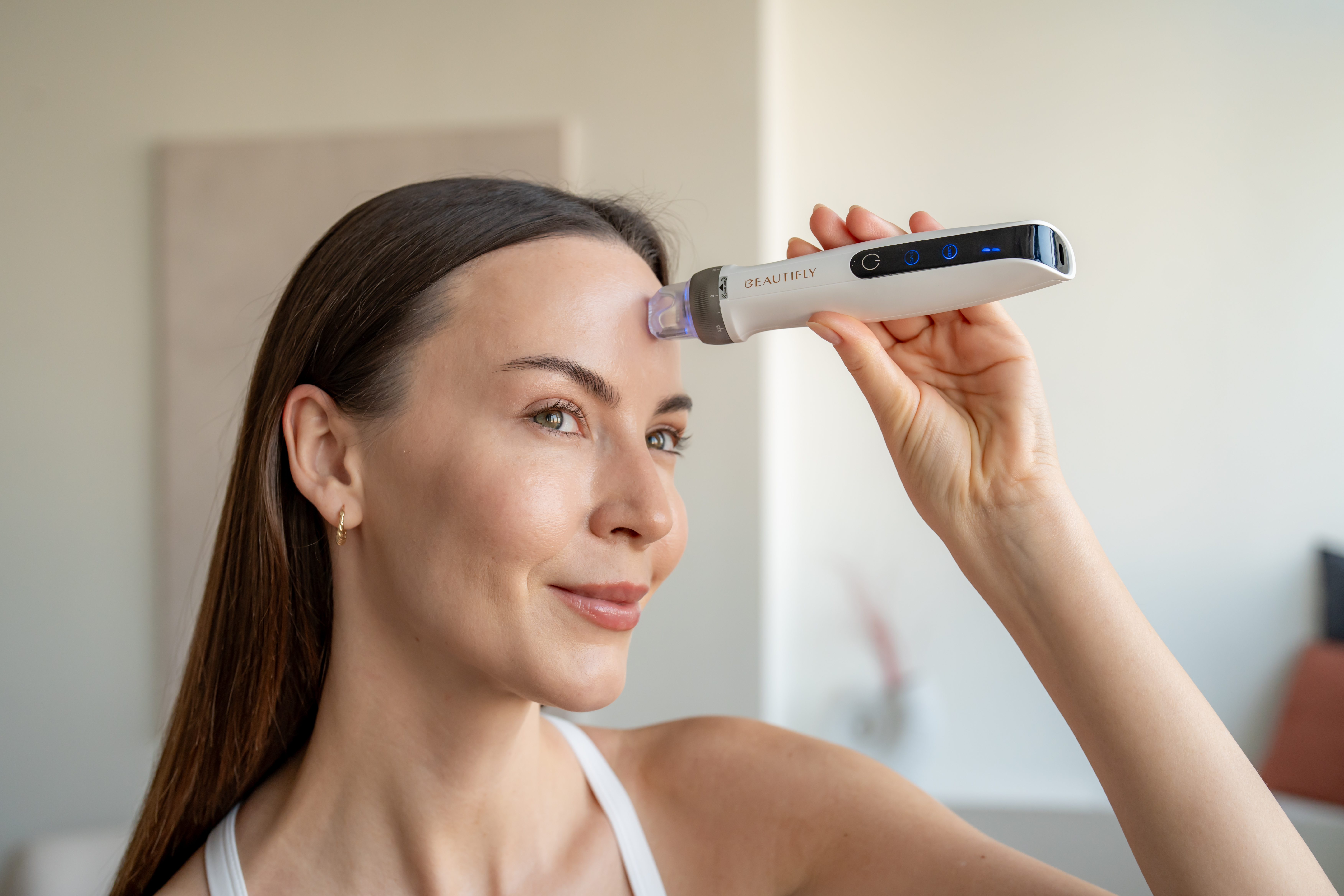Una donna tiene in mano un dispositivo cosmetico Beautifly bianco e lo applica sulla fronte.