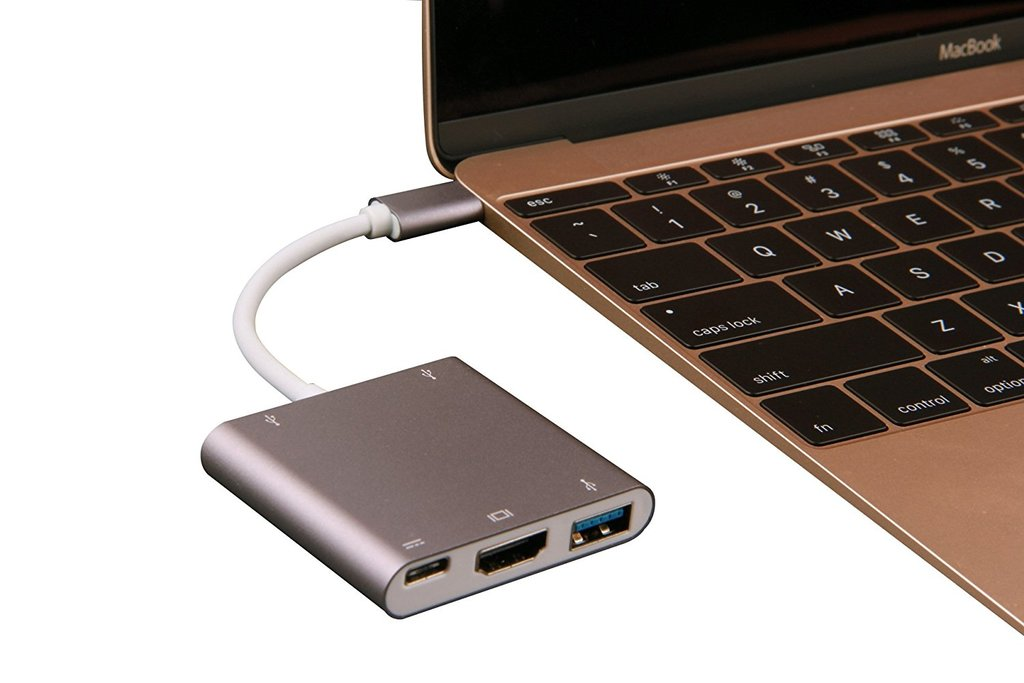 Egy szürke USB-C hub HDMI- és USB-portokkal csatlakozik egy aranyszínű MacBookhoz.