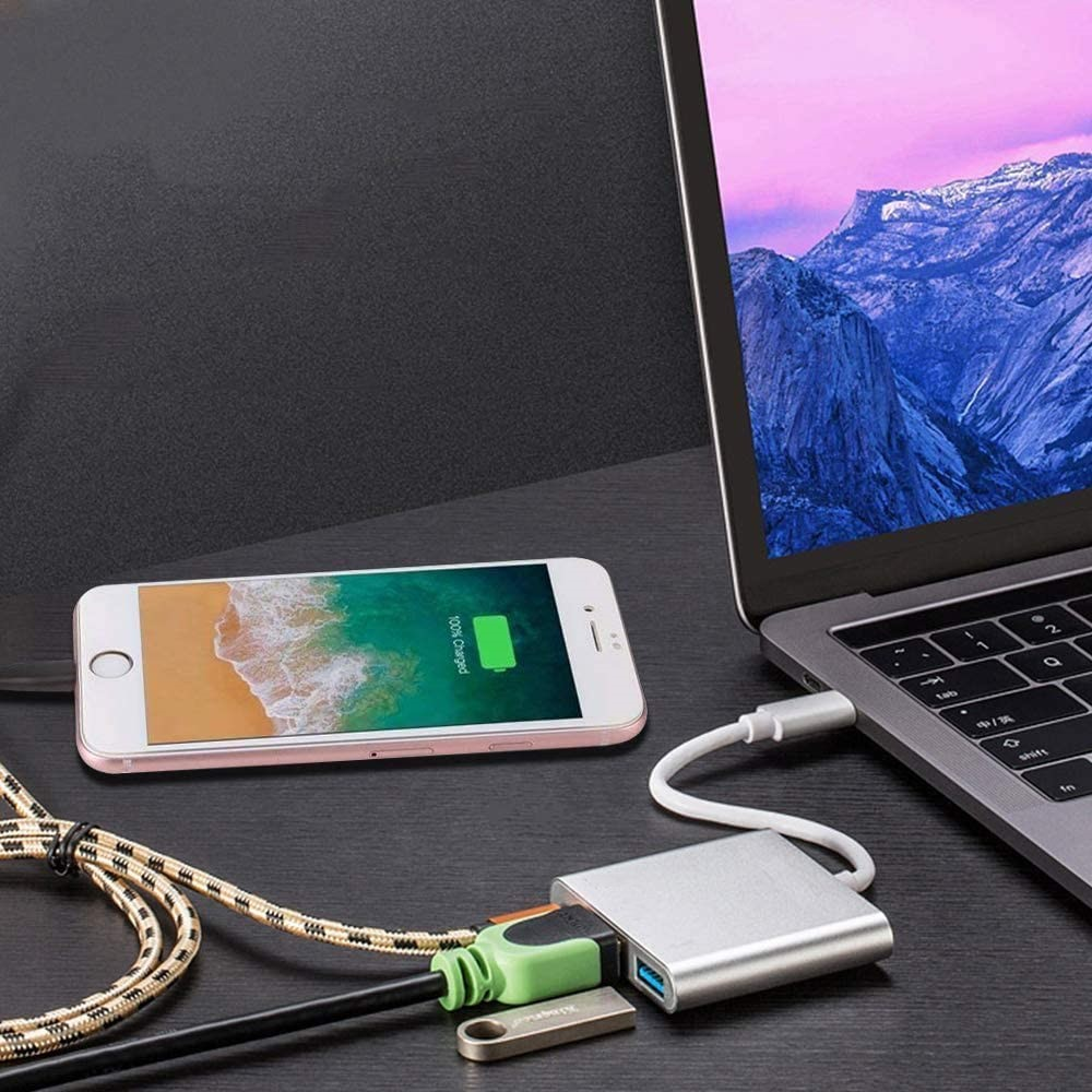 Egy okostelefon és egy USB-C hub csatlakoztatott kábelekkel egy laptop mellett fekszik az asztalon.