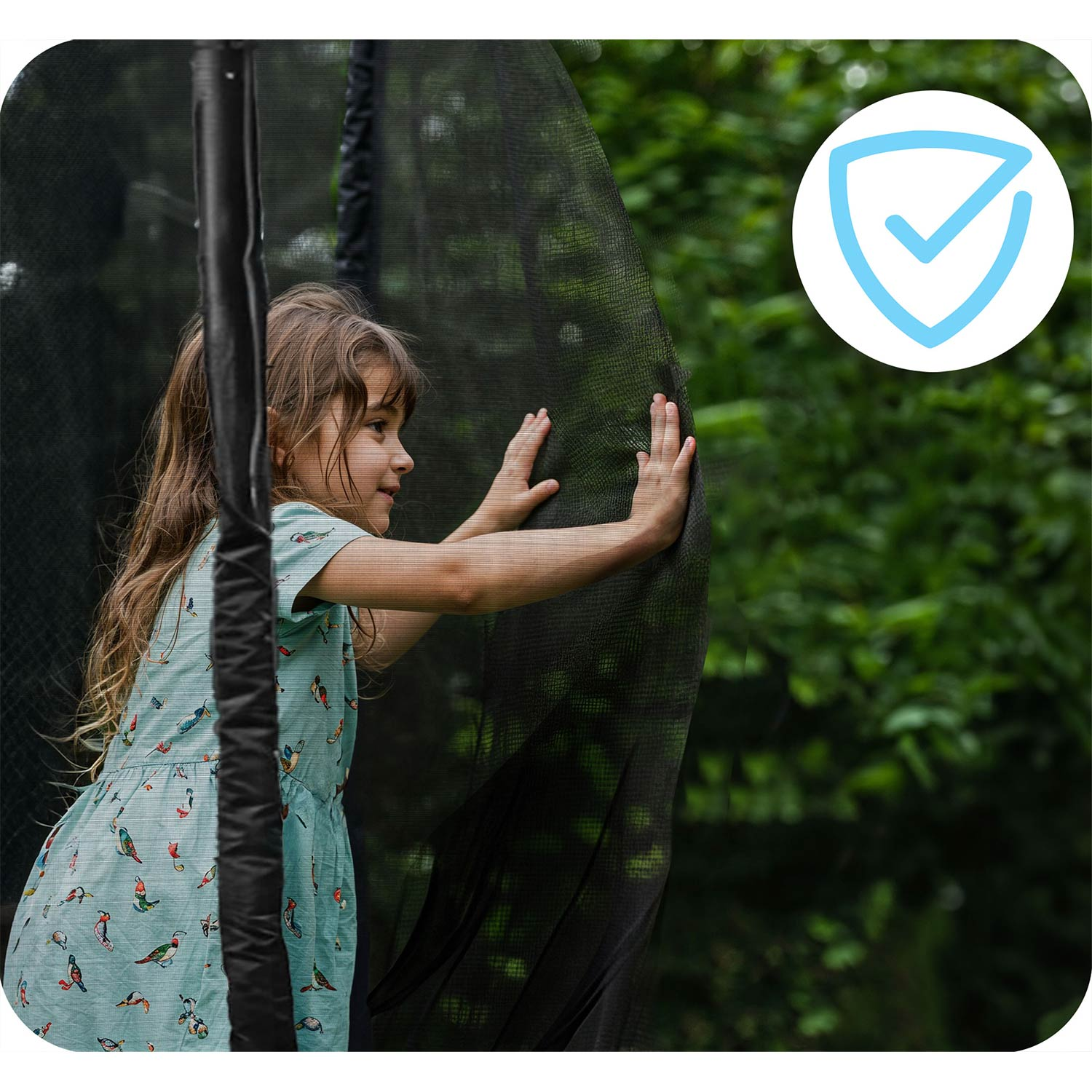Una bambina con un abito verde acqua si trova all'interno di un trampolino, con le mani contro la rete di sicurezza.