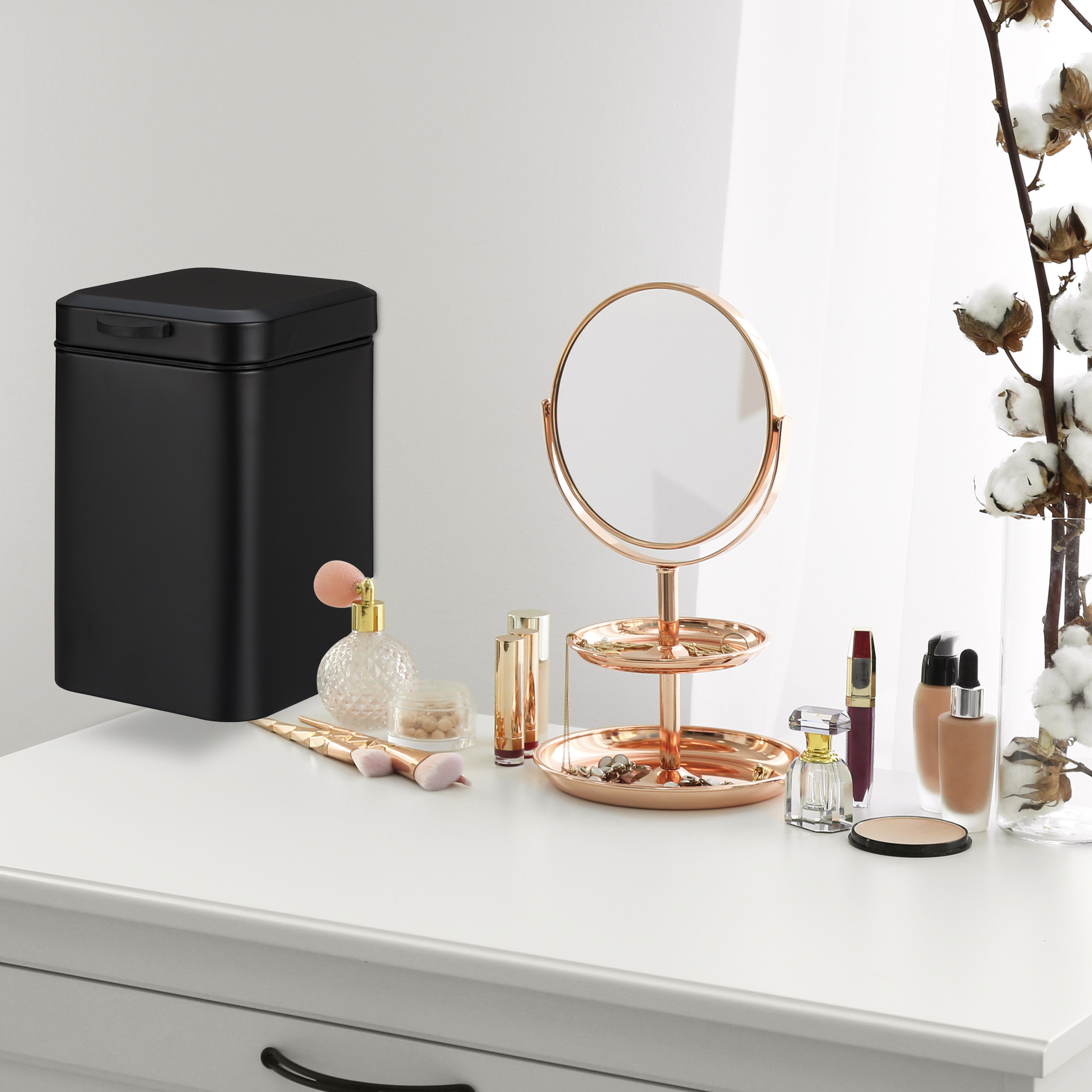 Ein schwarzer Eimer steht auf einem weißen Tisch neben einem Kosmetikspiegel und Make-up-Artikeln.