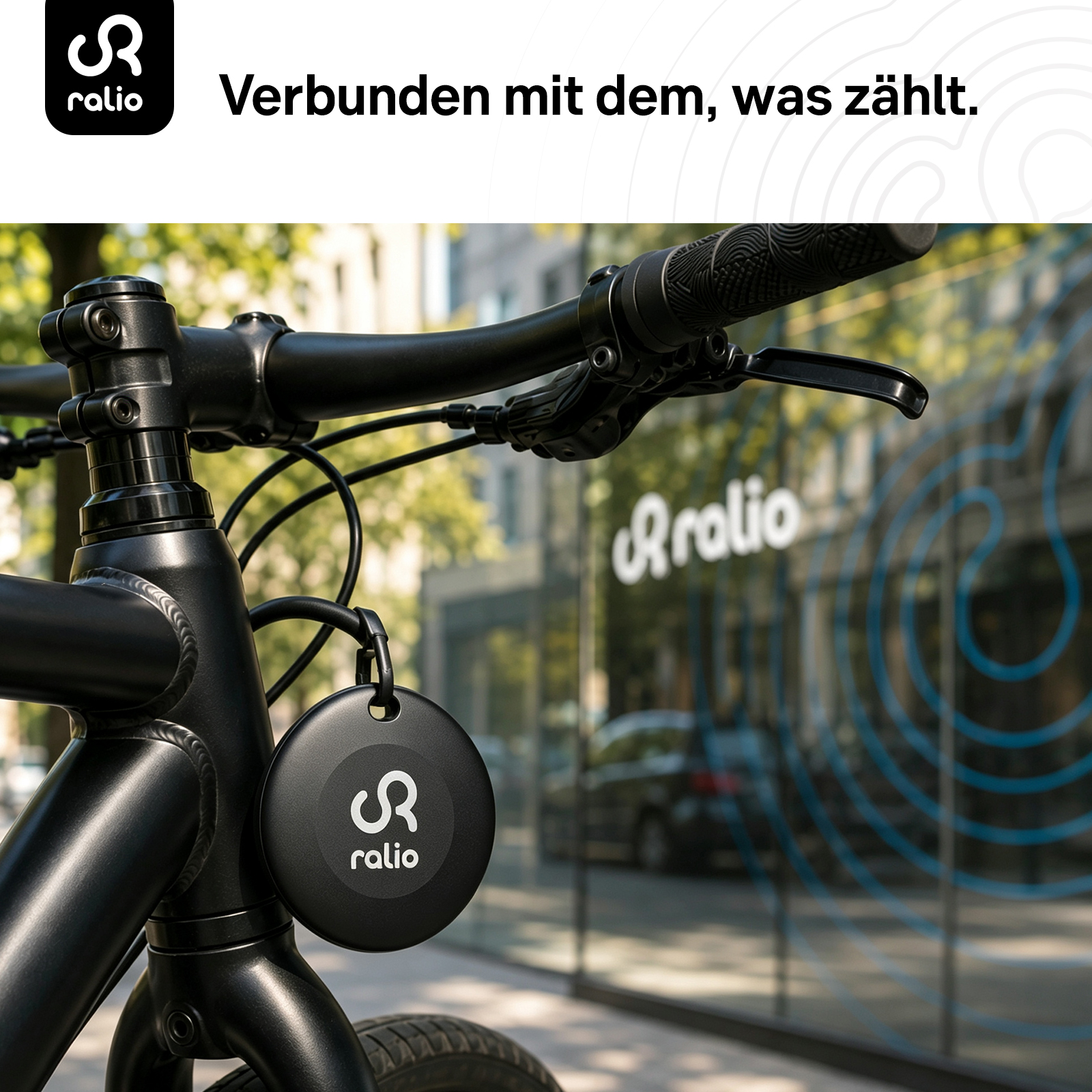 Ein schwarzes rali_o Ortungsgerät baumelt am Rahmen eines schwarzen Fahrrads vor einer Fensterscheibe.