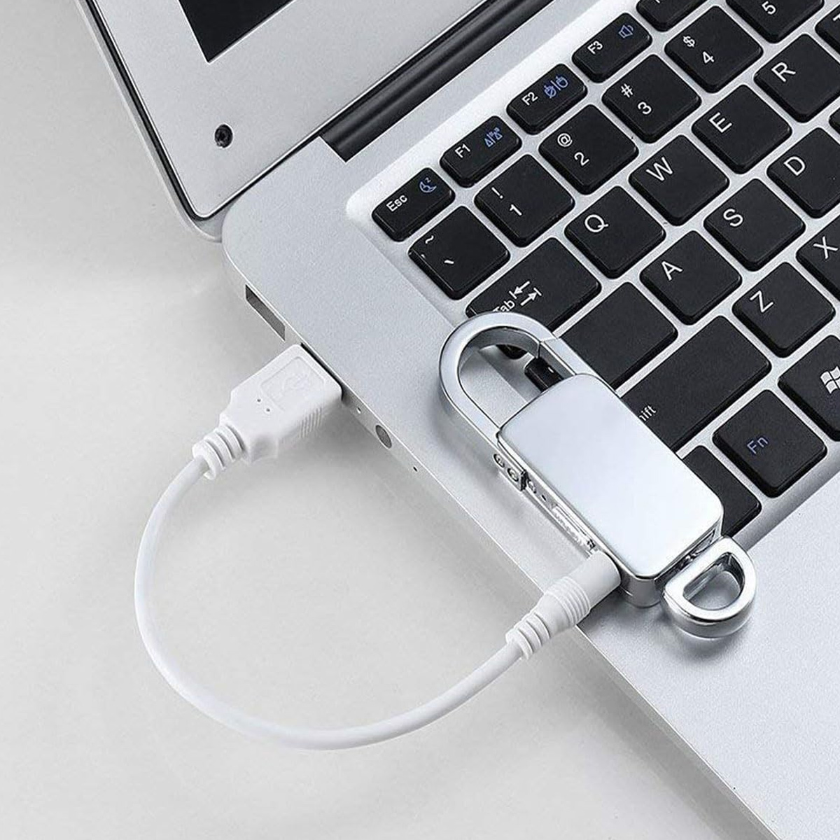 Eine silberne Laptoptastatur mit einem weißen Kabel im USB-Port und einem silbernen Schloss auf den Tasten.