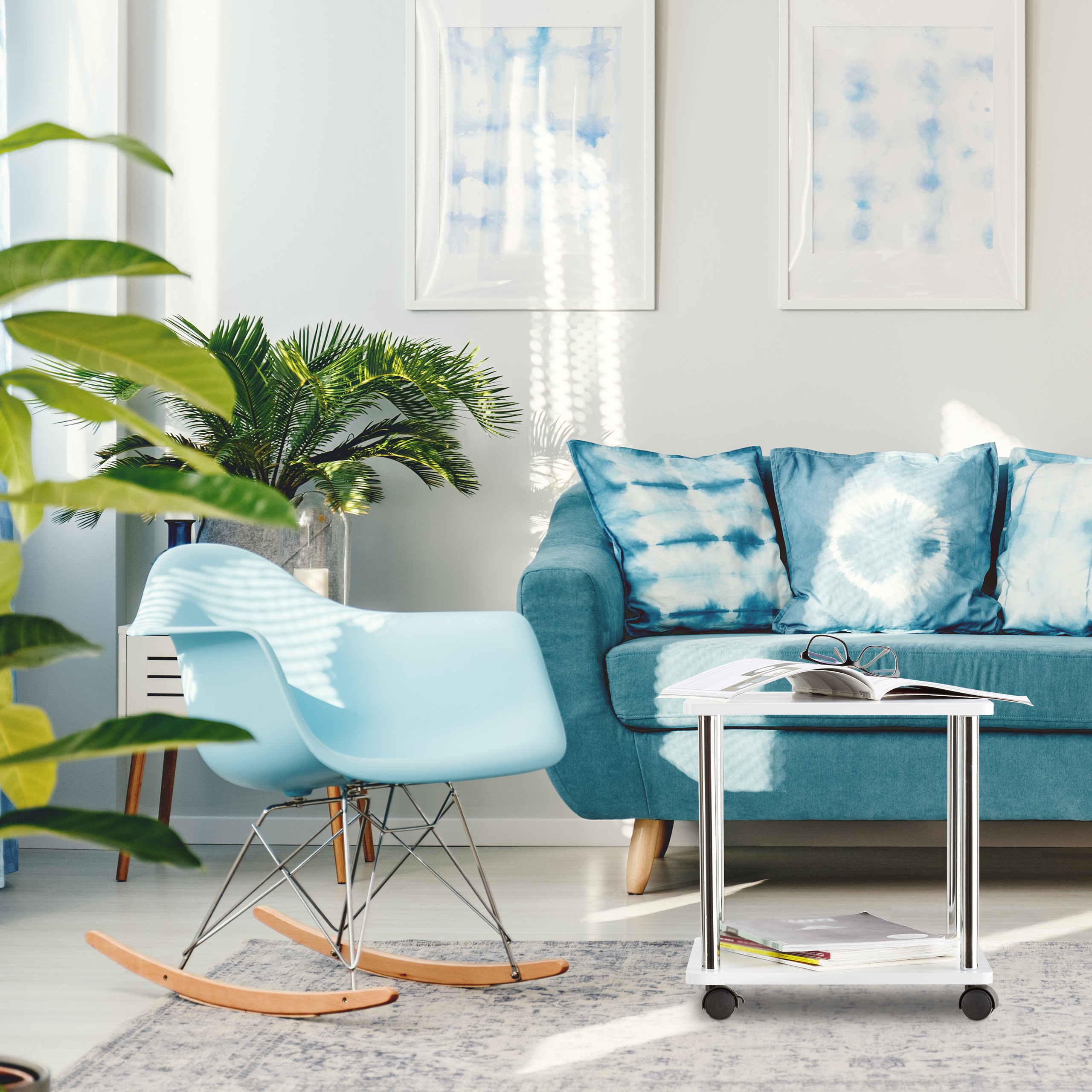 Ein hellblaues Wohnzimmer mit Sofa, Schaukelstuhl, kleinem Tisch und zwei blauen Bildern an der Wand.