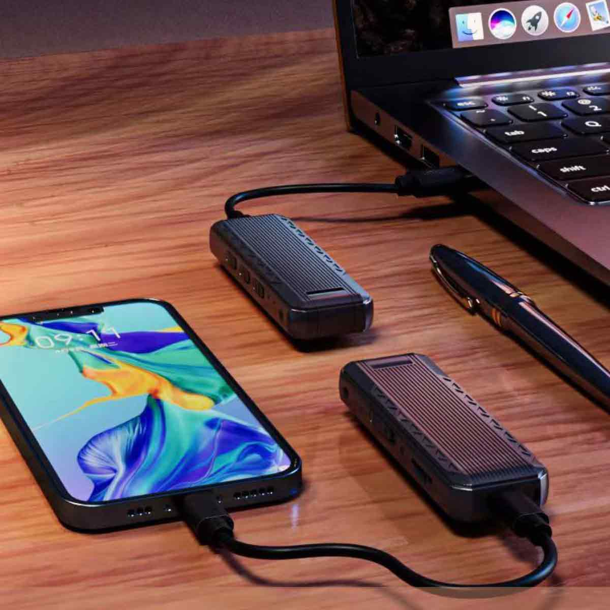 Auf einem Holztisch liegen ein Smartphone, ein Laptop, zwei schwarze SSD-Gehäuse und ein Stift.