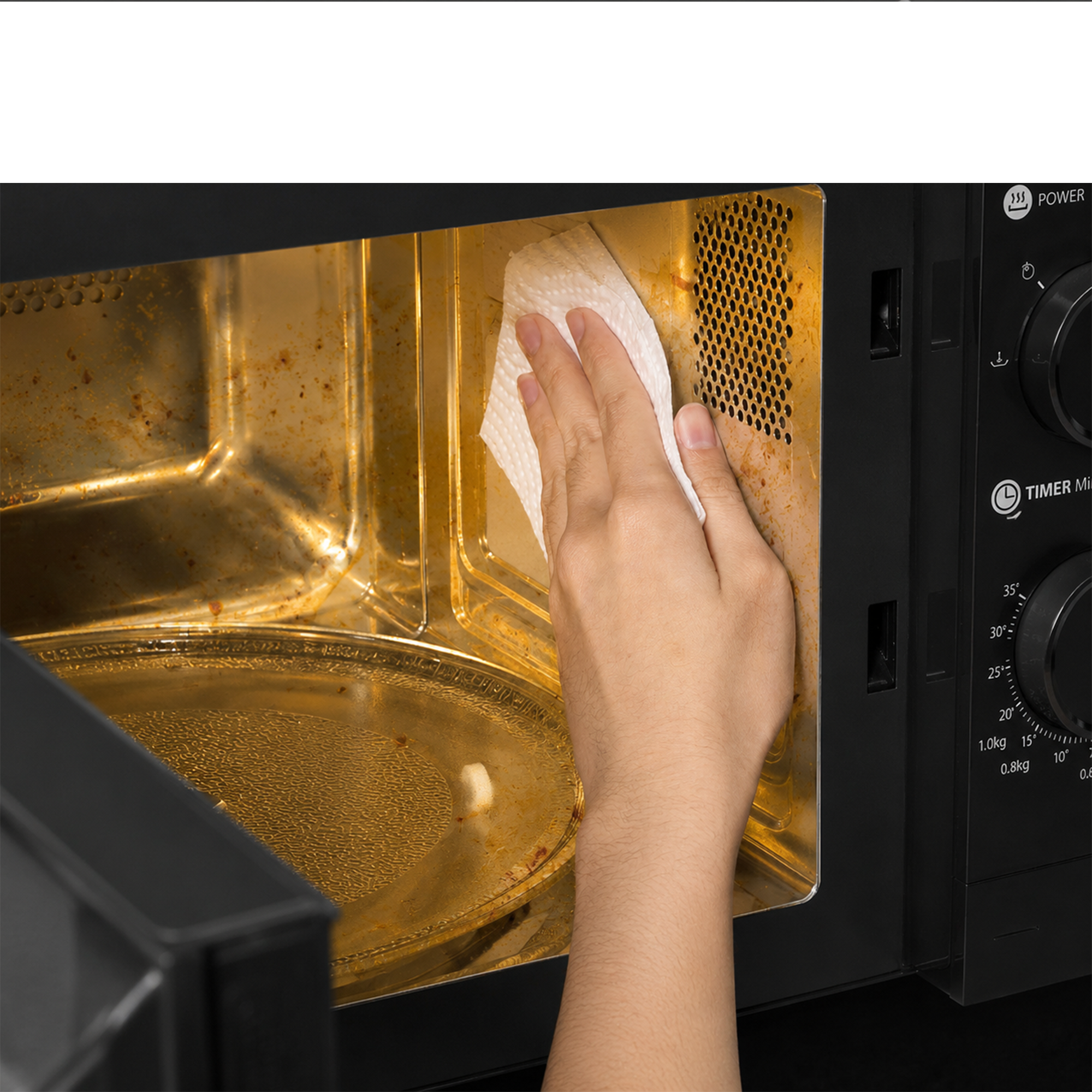 A hand uses a paper towel to wipe the dirty, grease-stained interior of a black microwave oven.