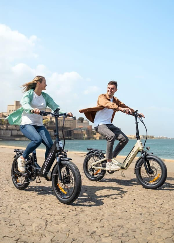 Una coppia si sorride mentre guida le bici elettriche lungo un sentiero costiero in una giornata di sole.