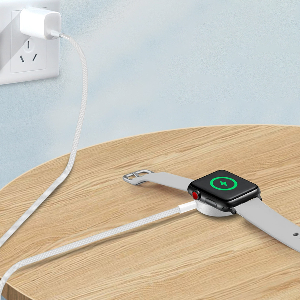 Eine Smartwatch liegt auf einem Holztisch und lädt über ein weißes Kabel auf, das mit einer Wandsteckdose verbunden ist.