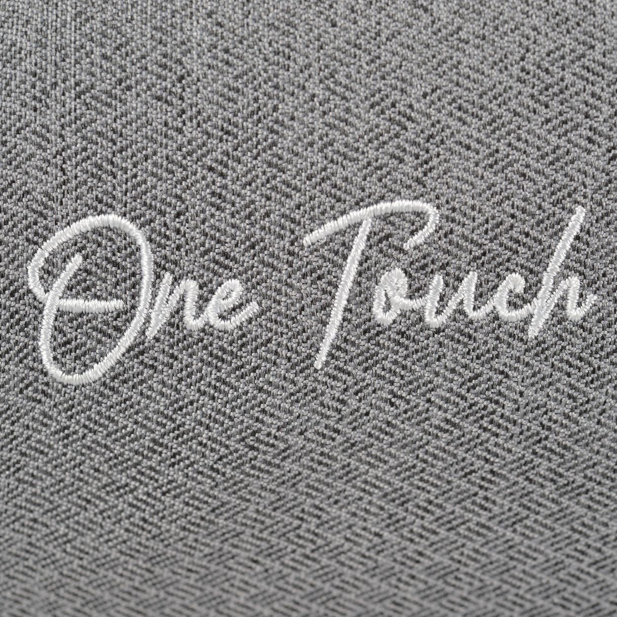 Nahaufnahme von weißem, gesticktem Text 'One Touch' auf strukturiertem, grauem Stoff.