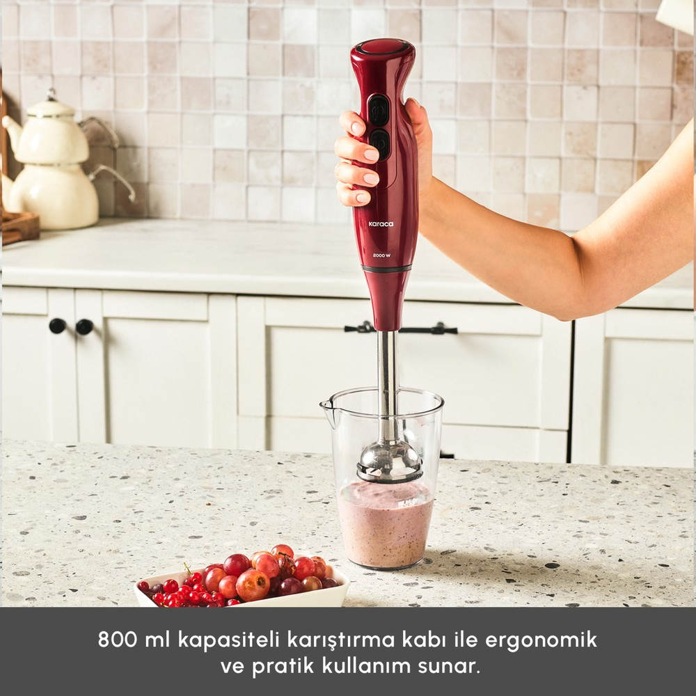 Bir el, kırmızı meyveli tezgahta, smoothie içeren ölçü kabı üzerinde kırmızı el blenderı tutuyor.