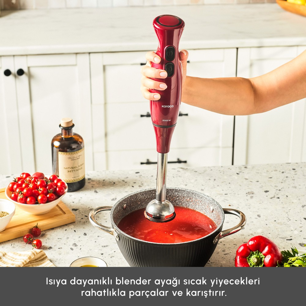 Bir mutfakta kırmızı çorba dolu tencerenin üzerinde el mikseri tutan bir el.