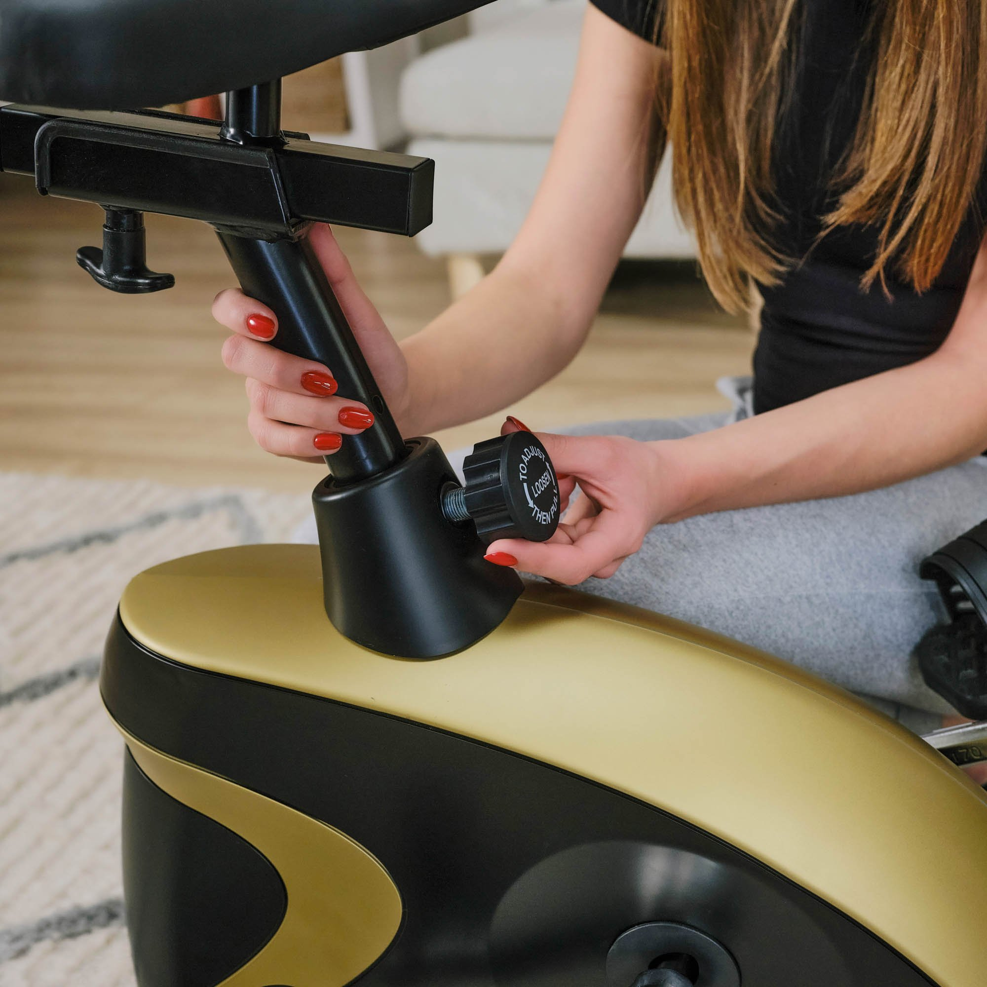 Eine Frau verstellt die Sitzhöhe an einem schwarz-goldenen Heimtrainer.