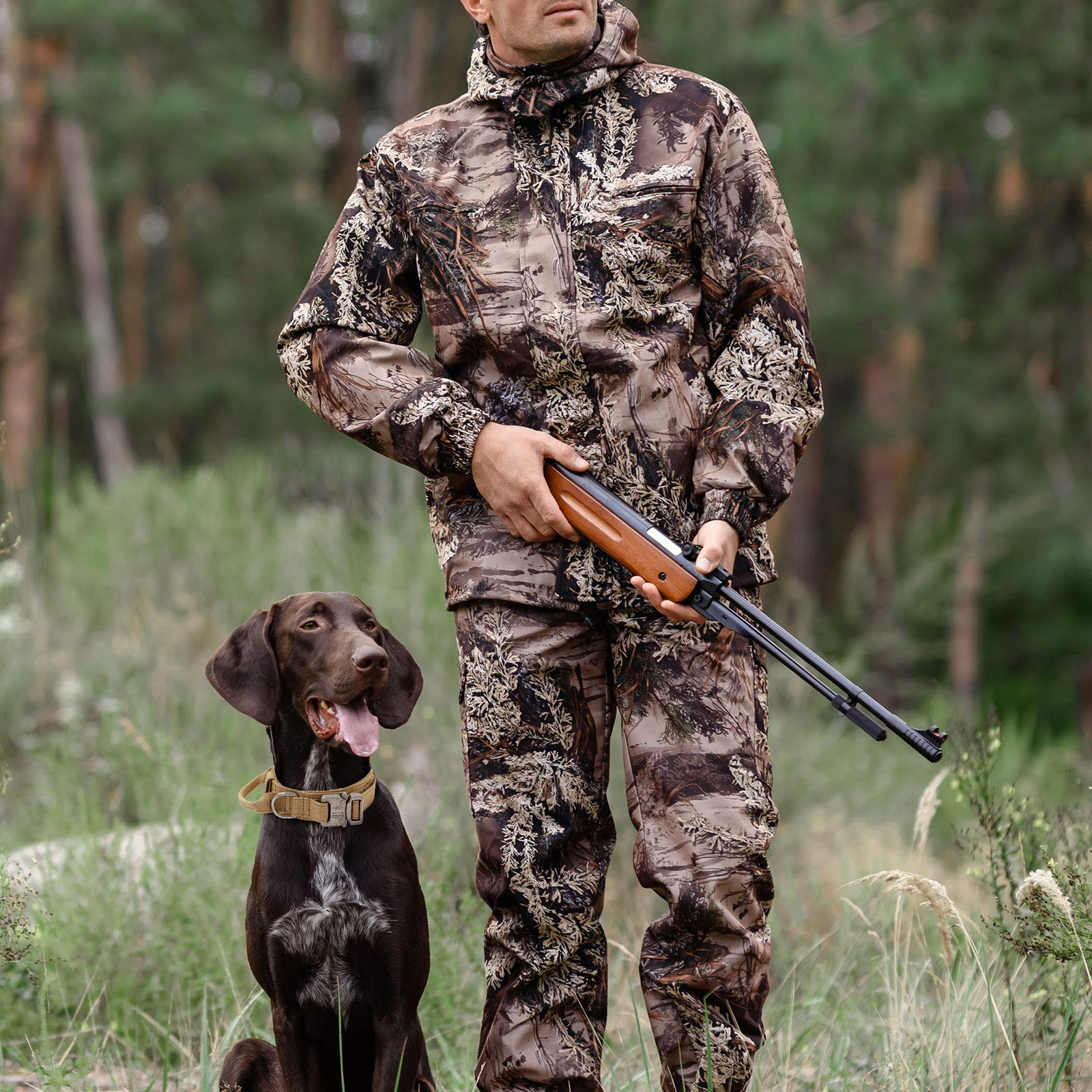 Ein Jäger in Tarnkleidung hält ein Gewehr, während sein brauner Hund mit gelbem Halsband im Gras sitzt.
