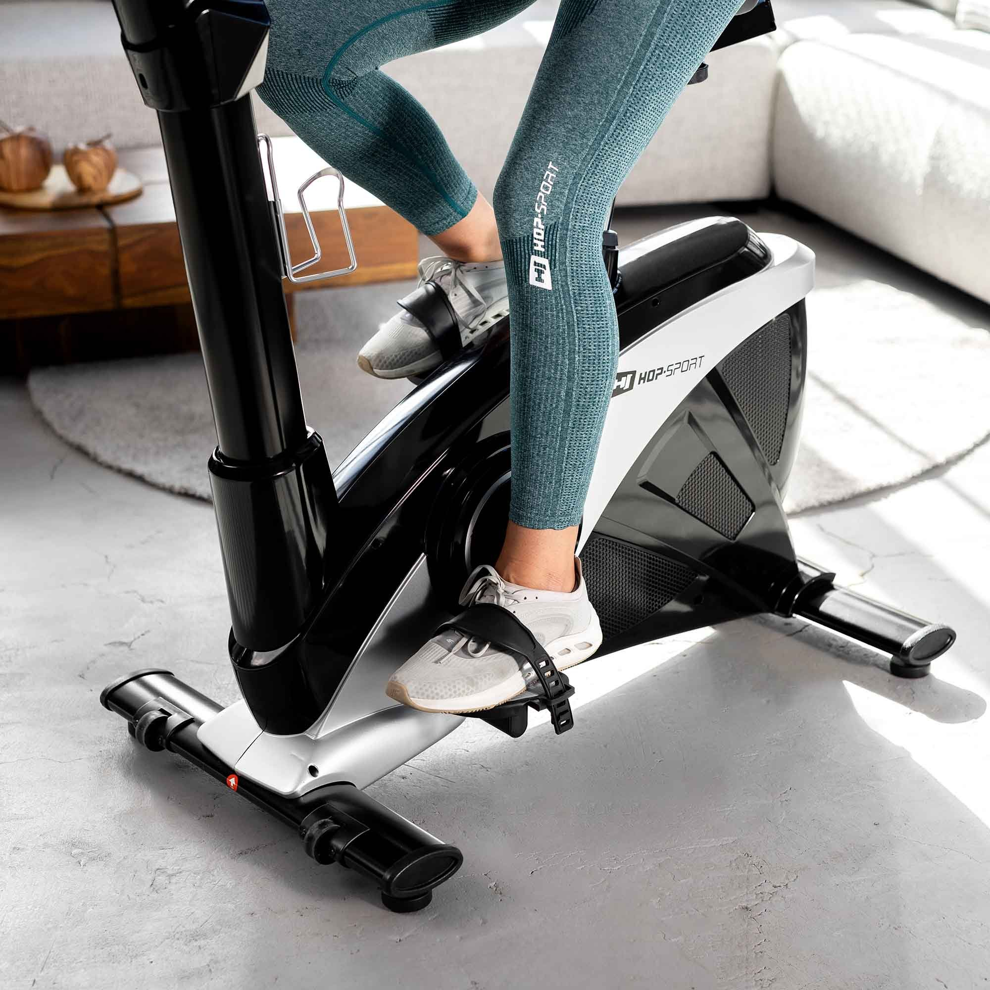 Person in blauen Leggings fährt auf einem schwarzen Hometrainer in einem hellen Raum.