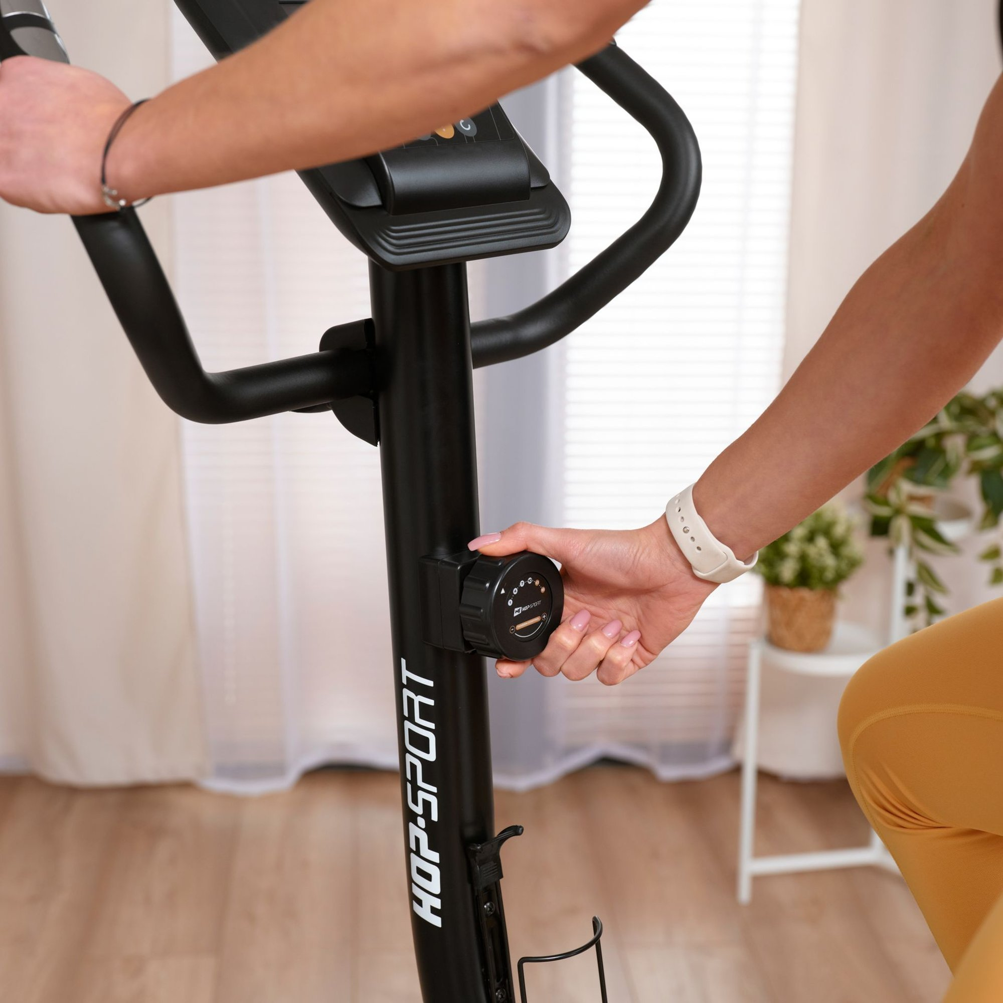 Eine Person sitzt auf einem schwarzen Heimtrainer und stellt den Widerstandsknopf ein.