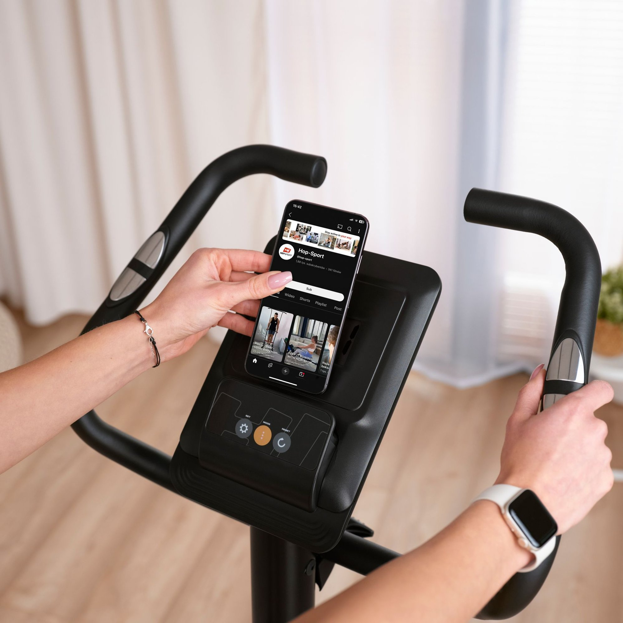 Eine Frau hält ein Smartphone an das Display eines Heimtrainers.