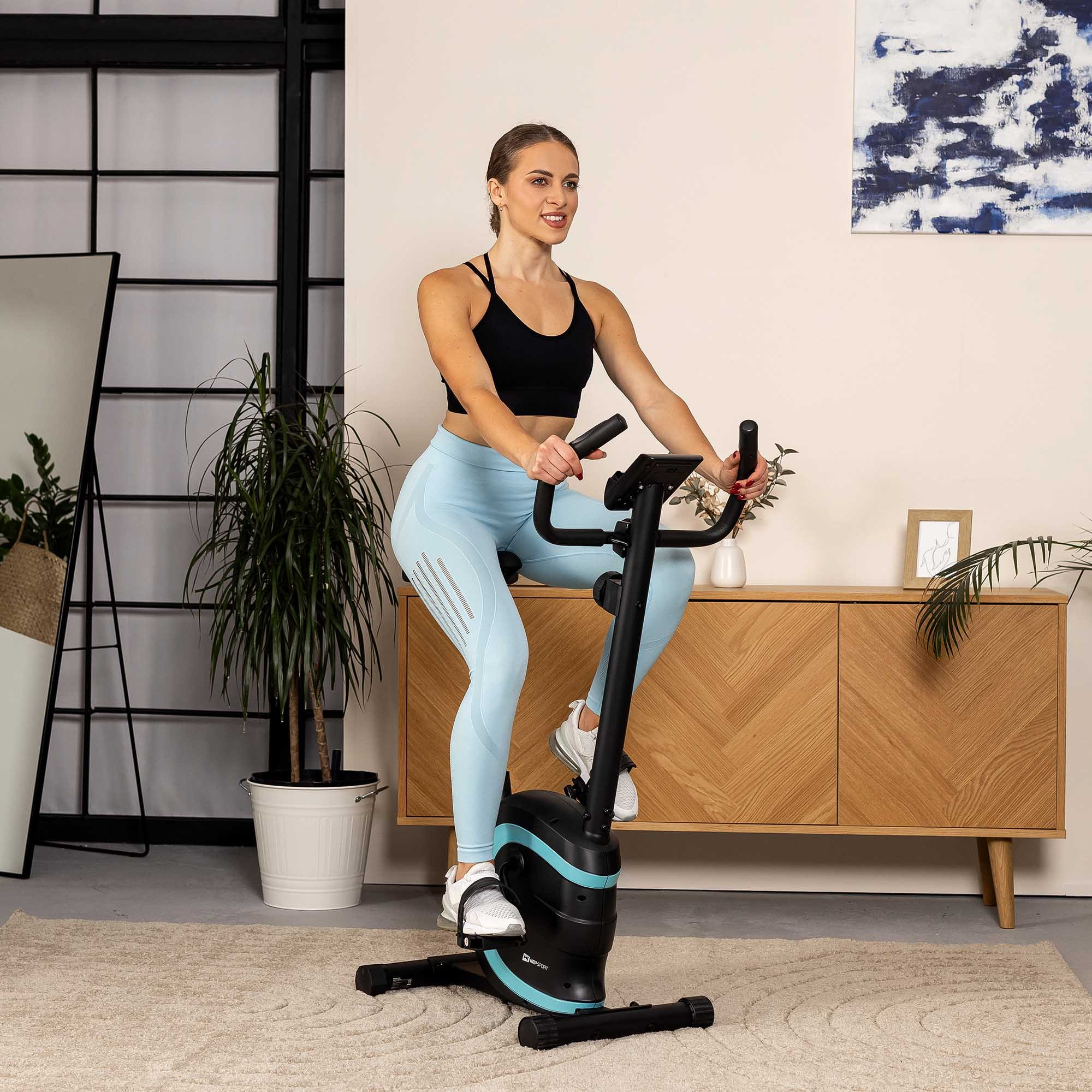 Eine Frau in Sportkleidung trainiert auf einem Heimtrainer in einem hellen, modern eingerichteten Raum.