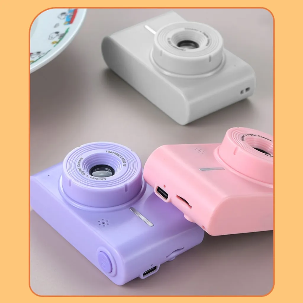 Drei kleine Kinderkameras in den Farben Grau, Lila und Rosa liegen auf einer grauen Oberfläche.