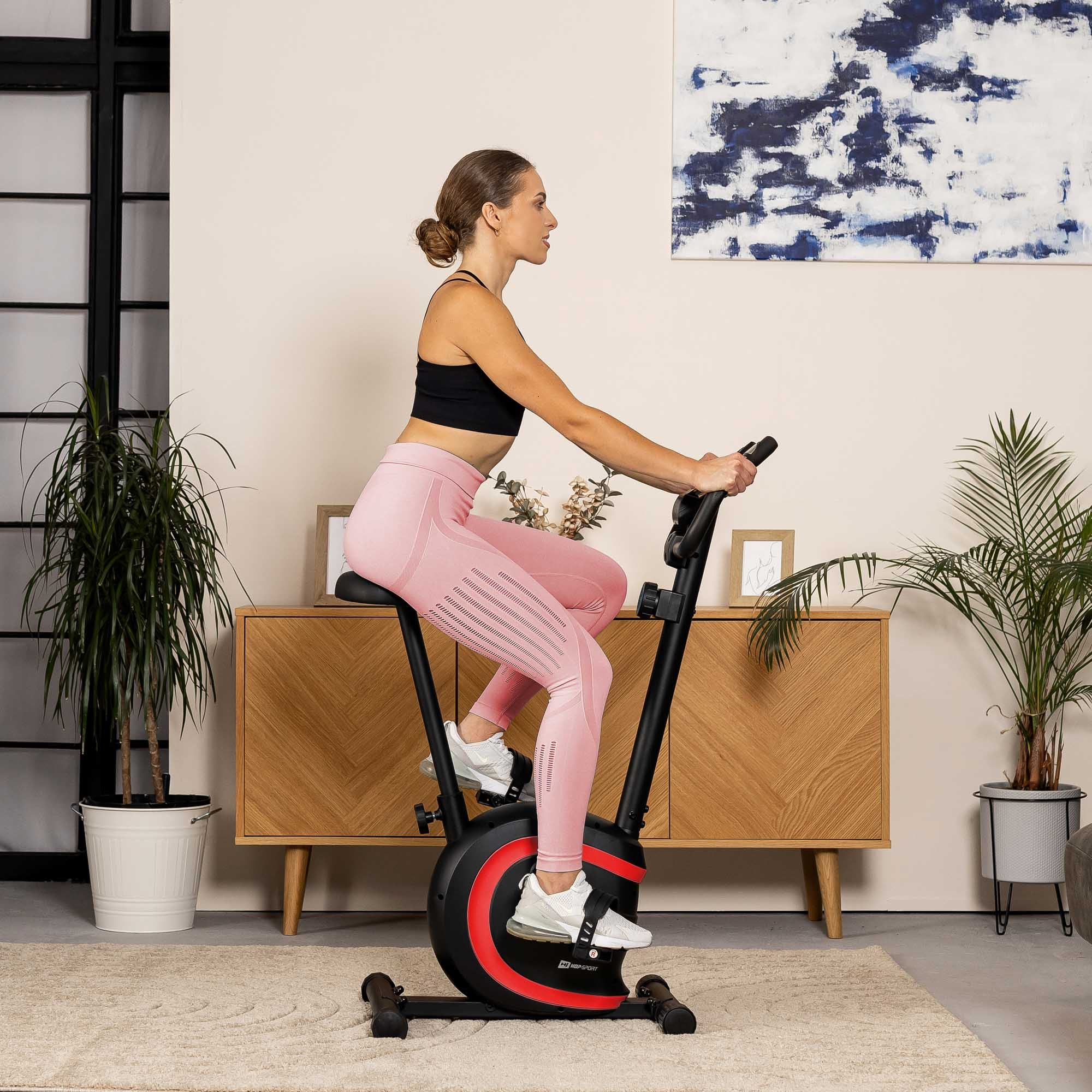 Eine Frau in Sportkleidung trainiert auf einem Heimtrainer in einem hellen Raum.