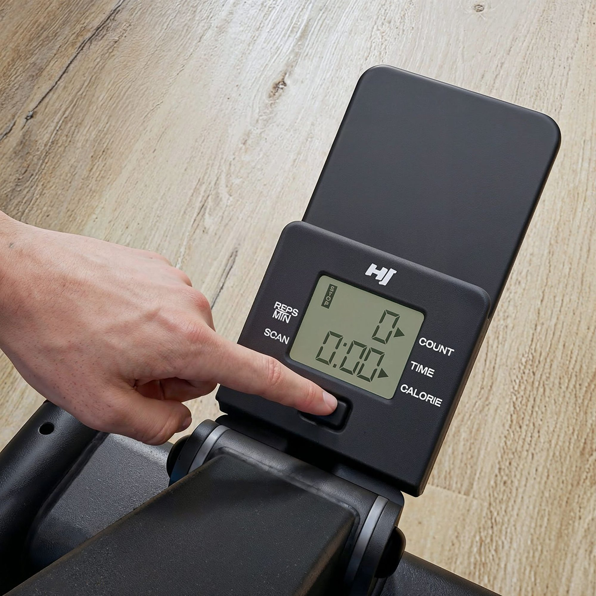 Eine Hand drückt die Taste auf einer schwarzen Fitnessgerätedisplay-Konsole mit Nullen.