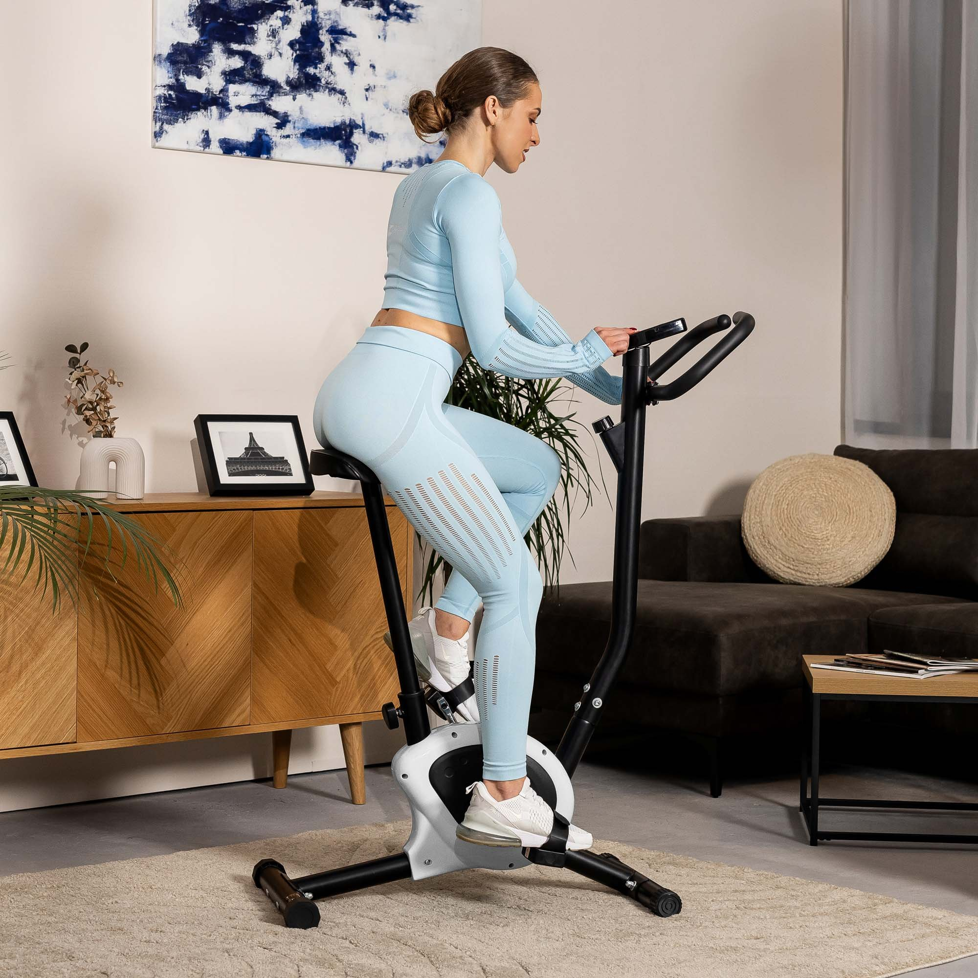 Eine Frau in blauer Sportkleidung trainiert zu Hause auf einem schwarzen Heimtrainer.