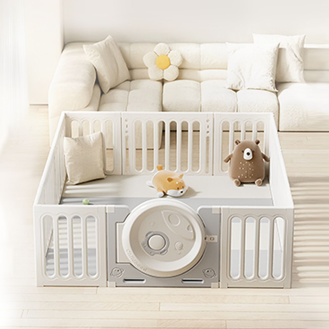 Ein weißer Baby-Laufstall mit Kuscheltieren steht auf Holzboden vor einem weißen Sofa.
