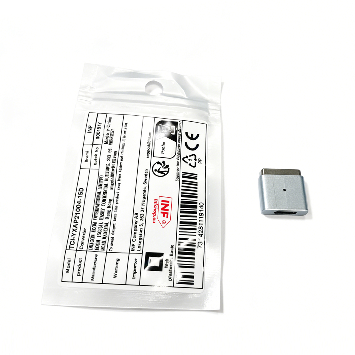 Ein kleiner silberner Magnetadapter liegt neben einer durchsichtigen Plastiktüte mit einem gedruckten Produktetikett.